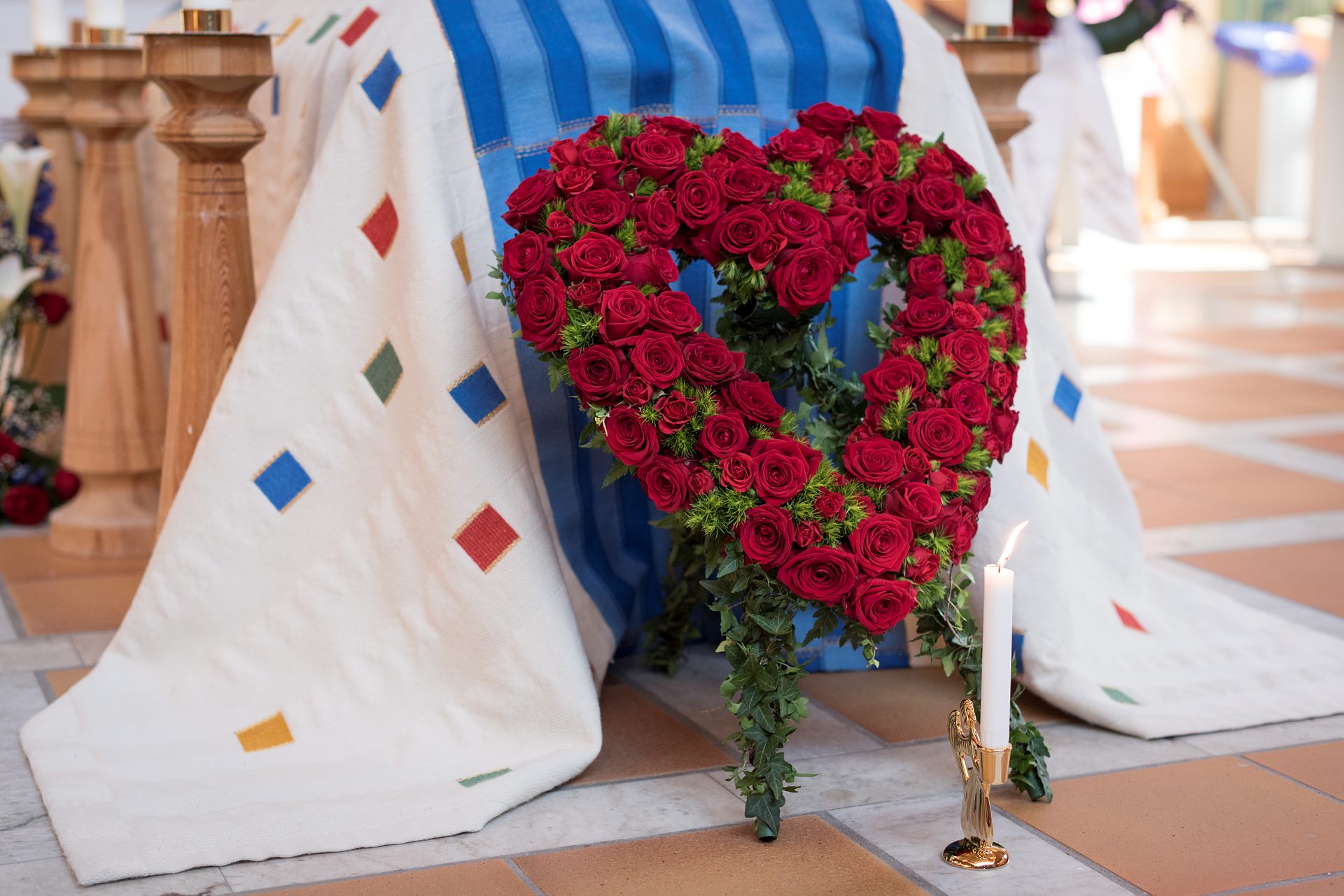 En begravningskrans i form av ett stort hjärta med rosor vilar mot en kista.