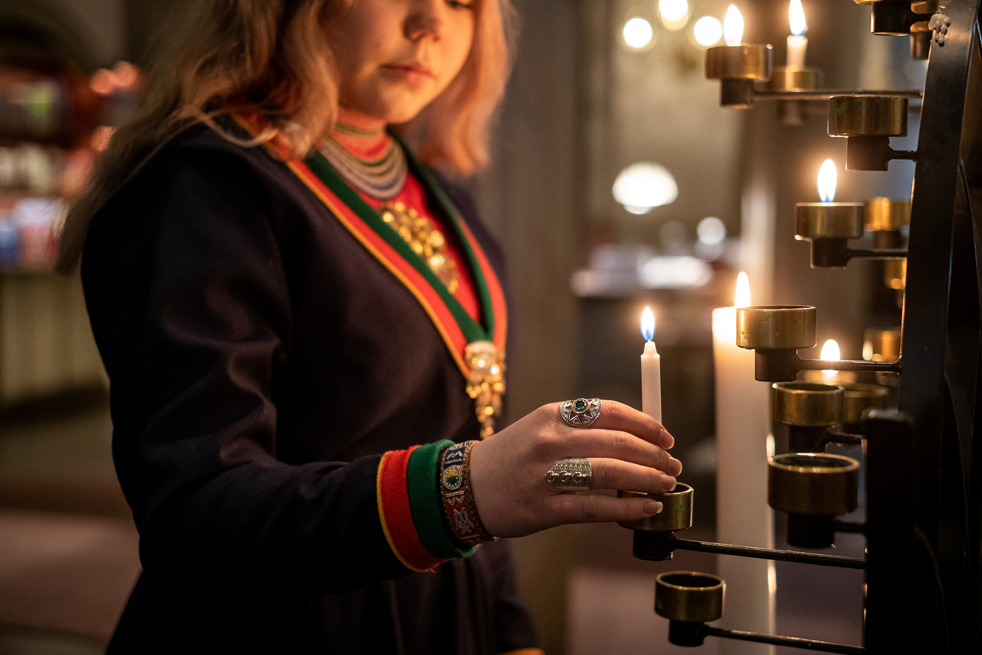 Flicka i samedräkt tänder ljus i ljusbäraren.