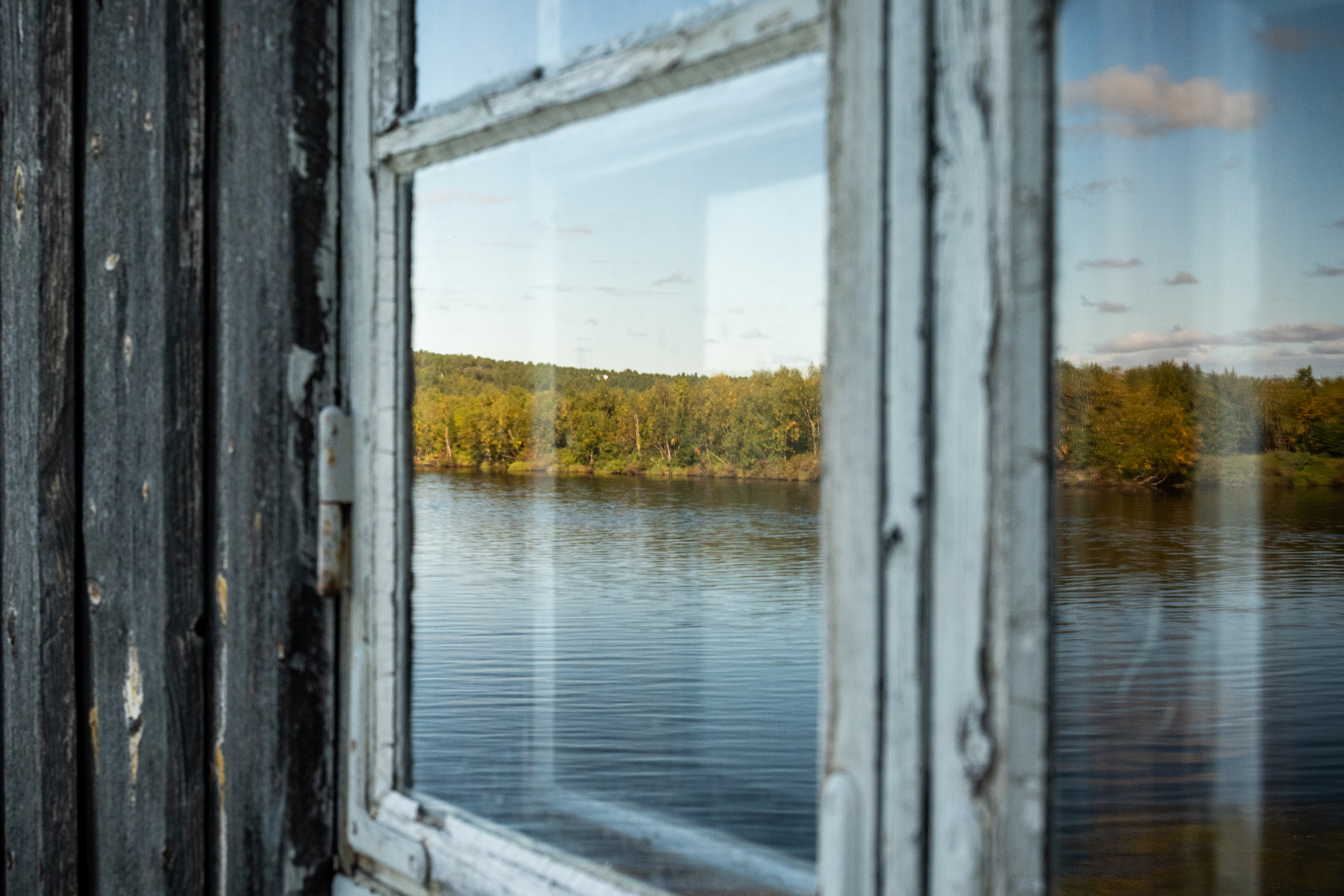 Ett landskap med en sjö speglas i fönstret på en grå trästuga.