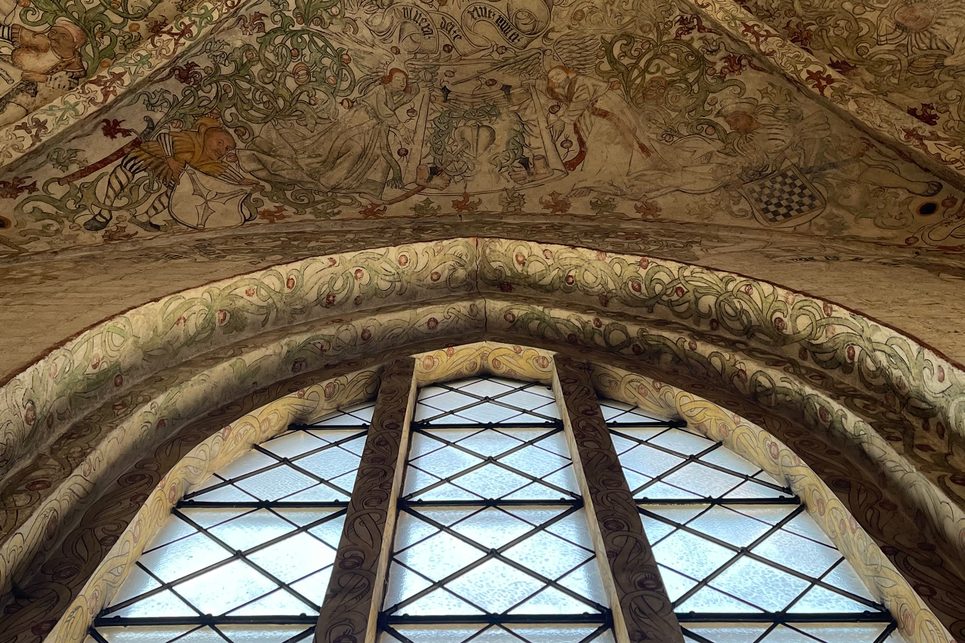 Bågformat fönster med spröjs och ovanför medeltida kalkmålningar.