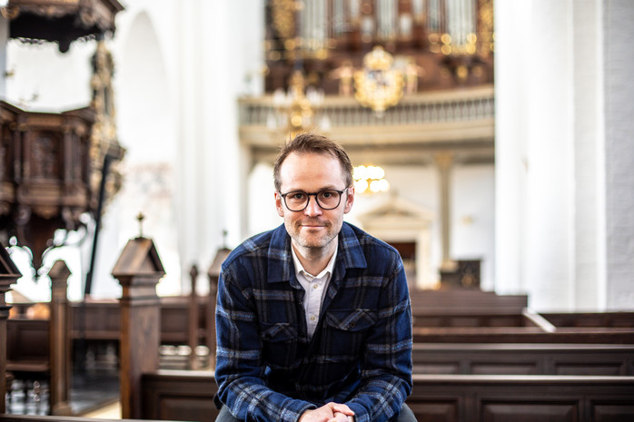 Man sittande på kyrkbänk lätt framåtlutad i rutig skjorta