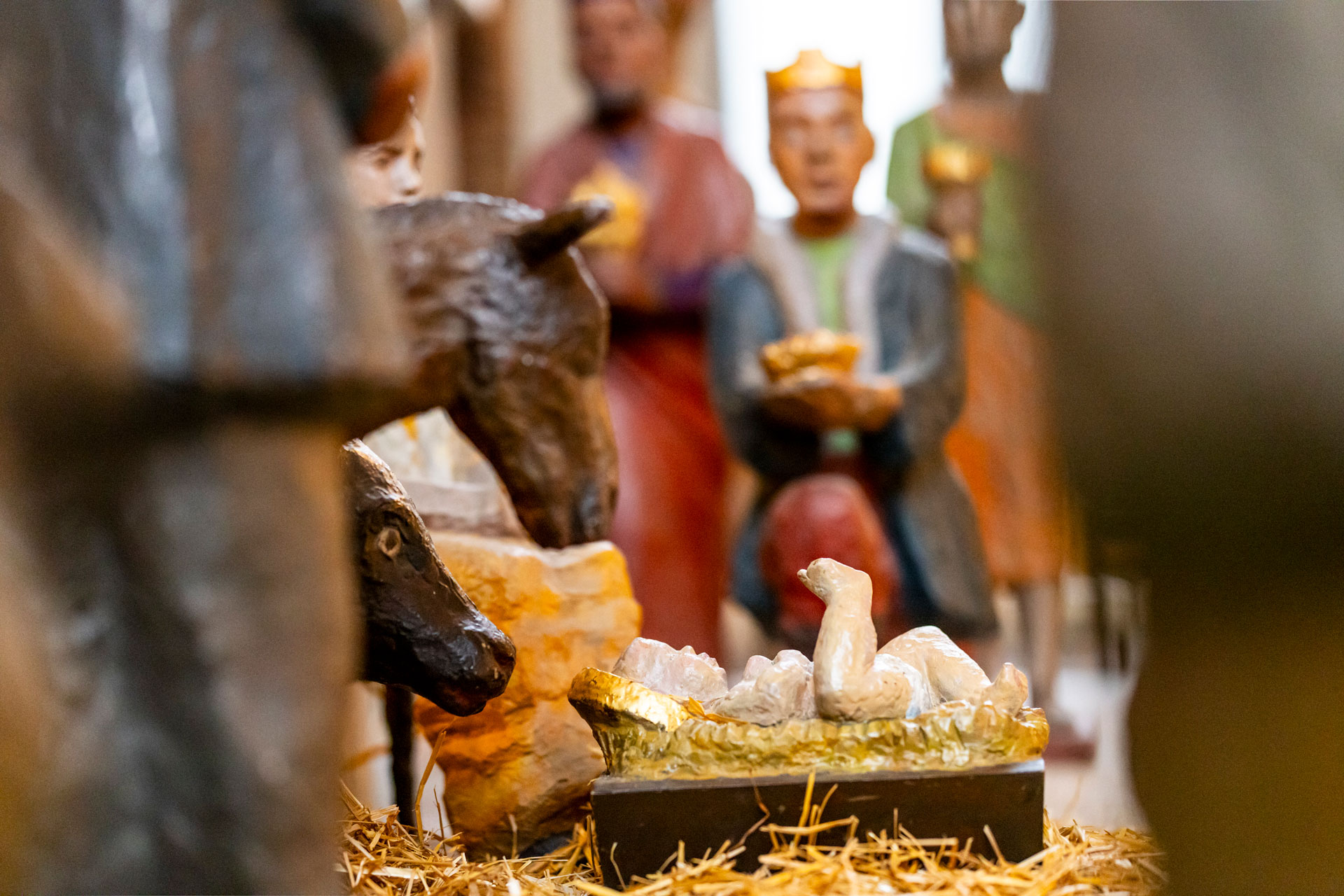 En något diffus bild som har fokus på ett litet barn i krubba på halm, åsna, oxe och tre män som bär gåvor.