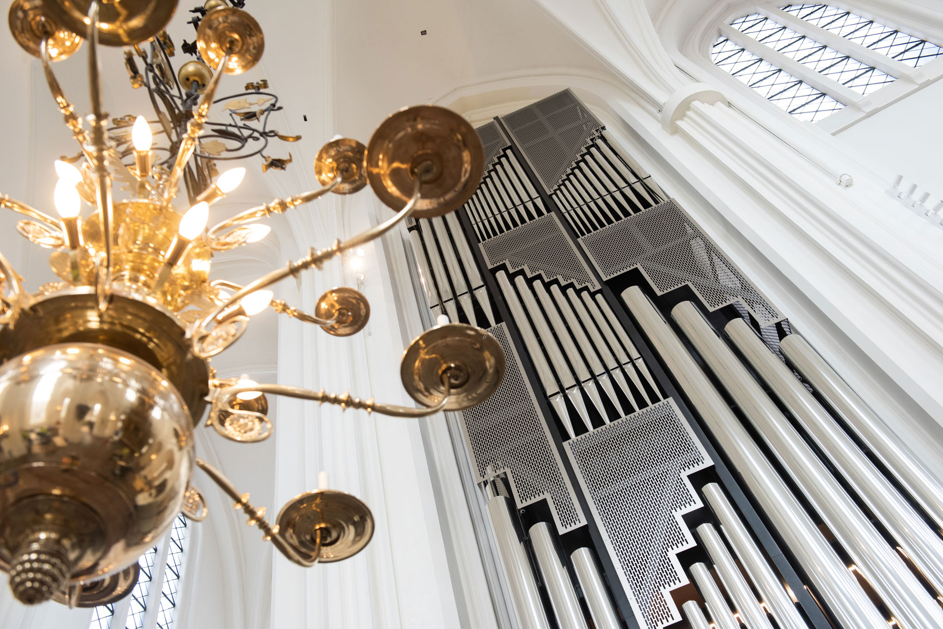 Orgelpipor under höga vita kyrkvalv samt stor takkrona.
