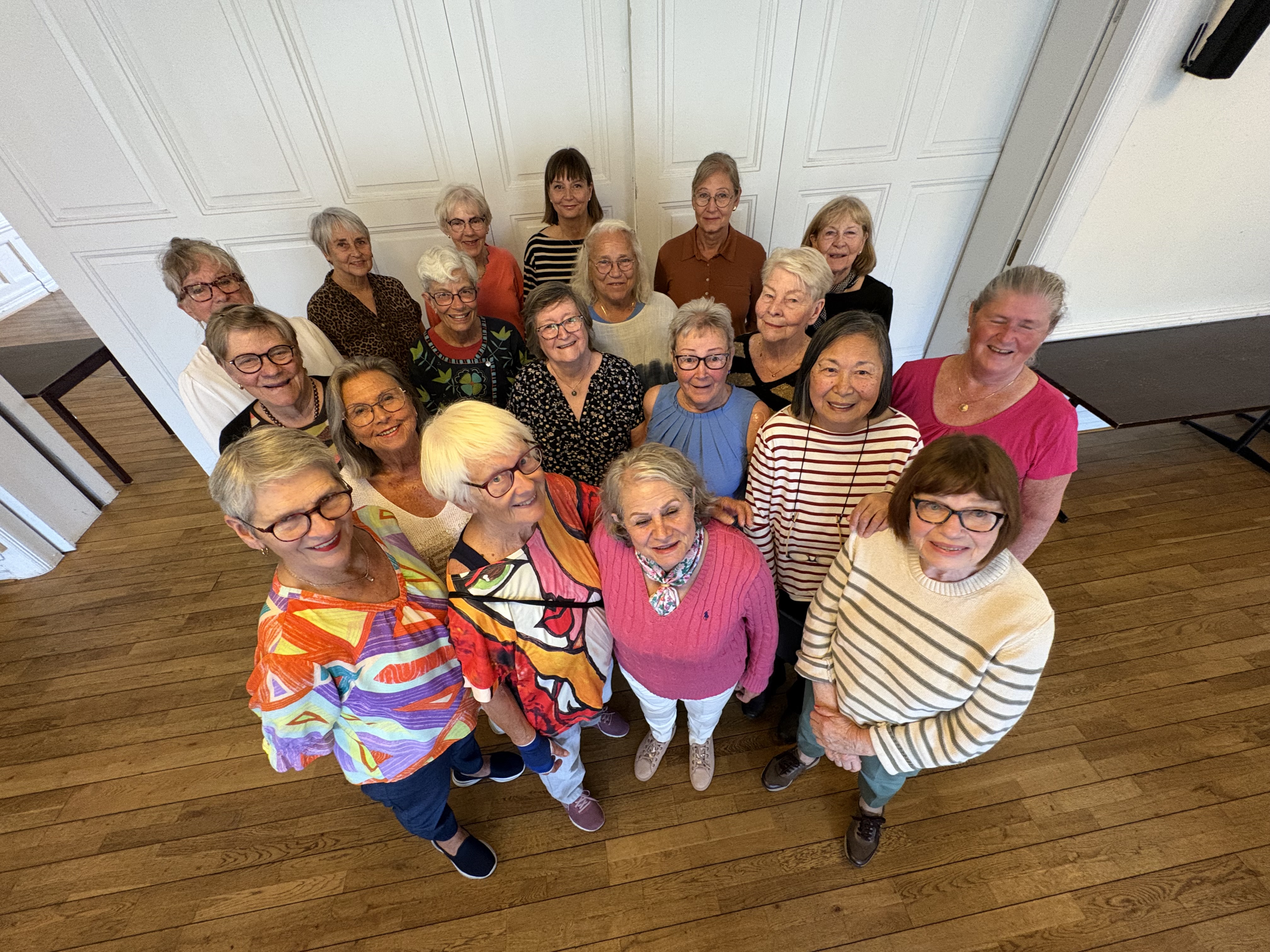 Grupp av äldre kvinnor stående framför en vit vikvägg