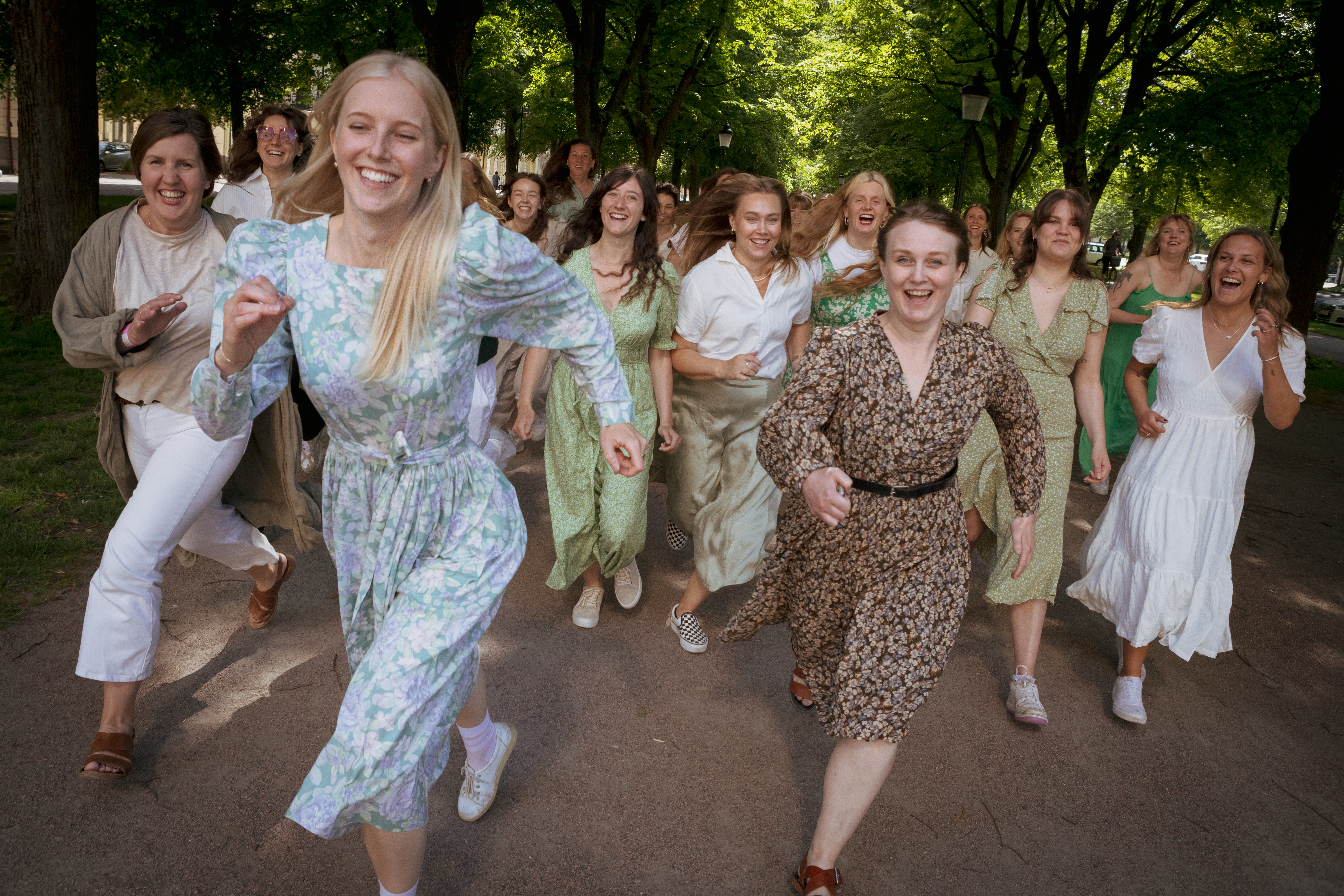 Grupp av kvinnor i sommarklänningar springer i en grön allé
