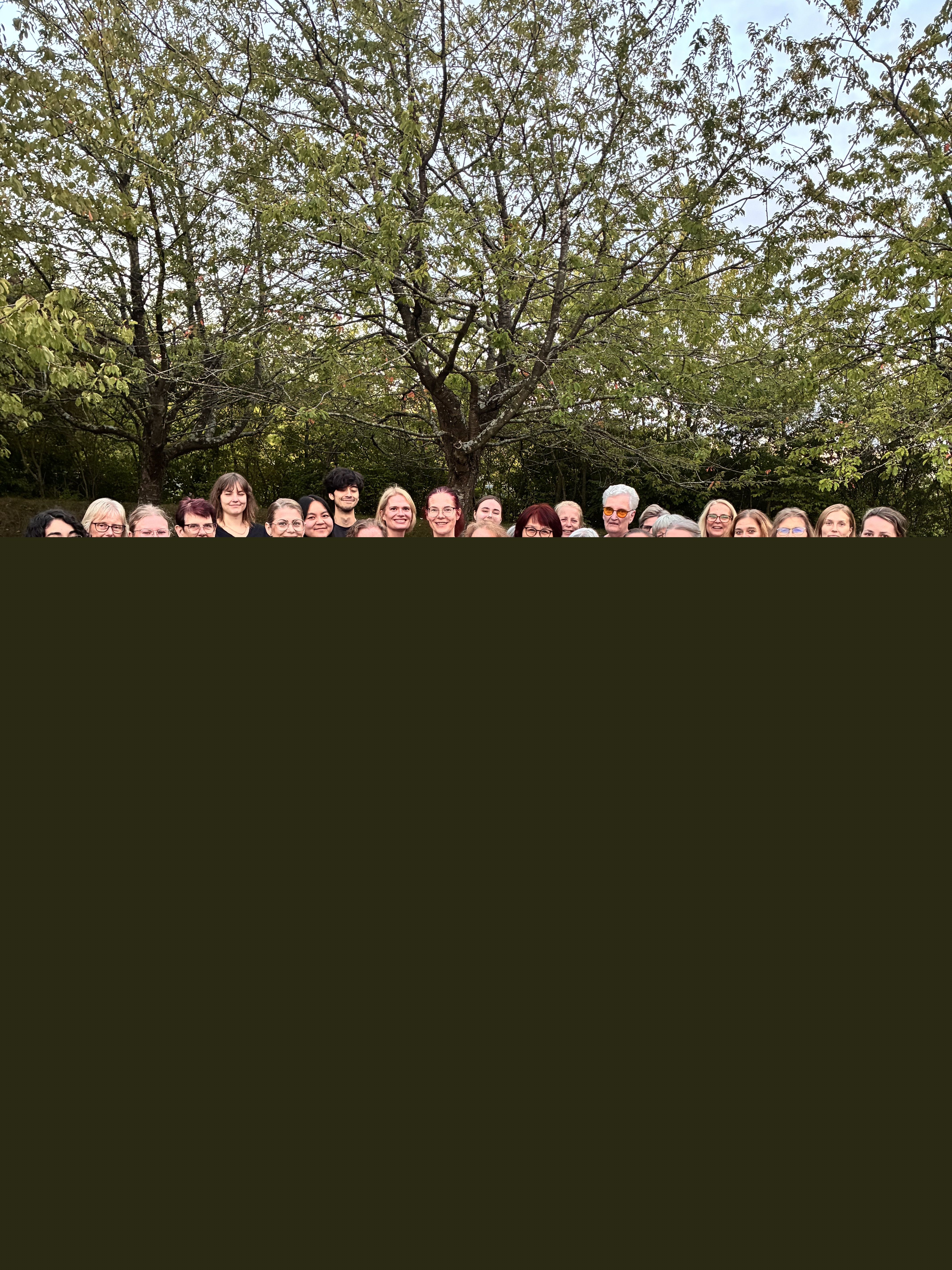 Grupp av kvinnor och män stående på en grön gräsmatta med träd i bakgrunden.