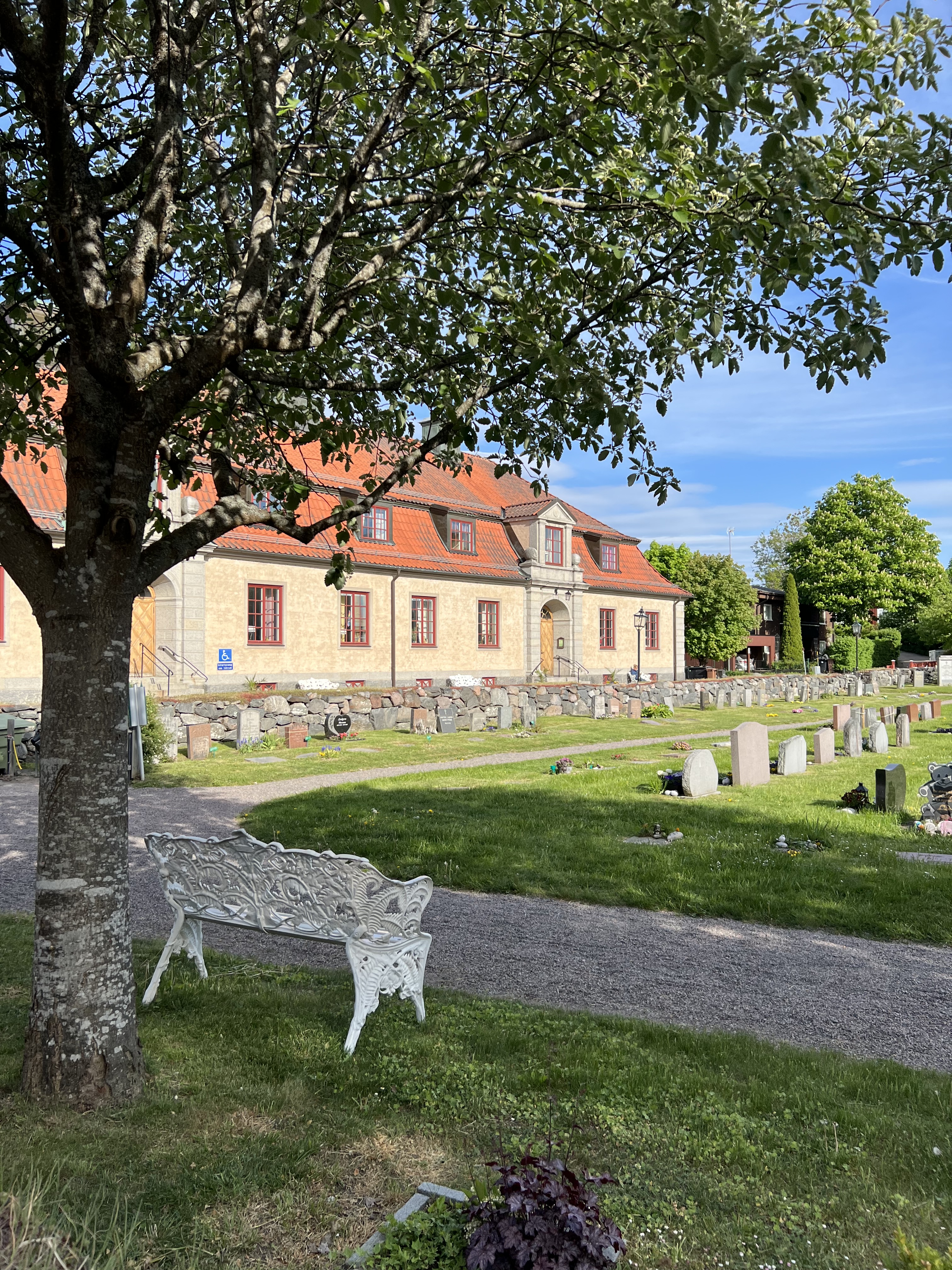 Östhammars församlingsgård med en bänk och gravar samt mur i förgrunden. 