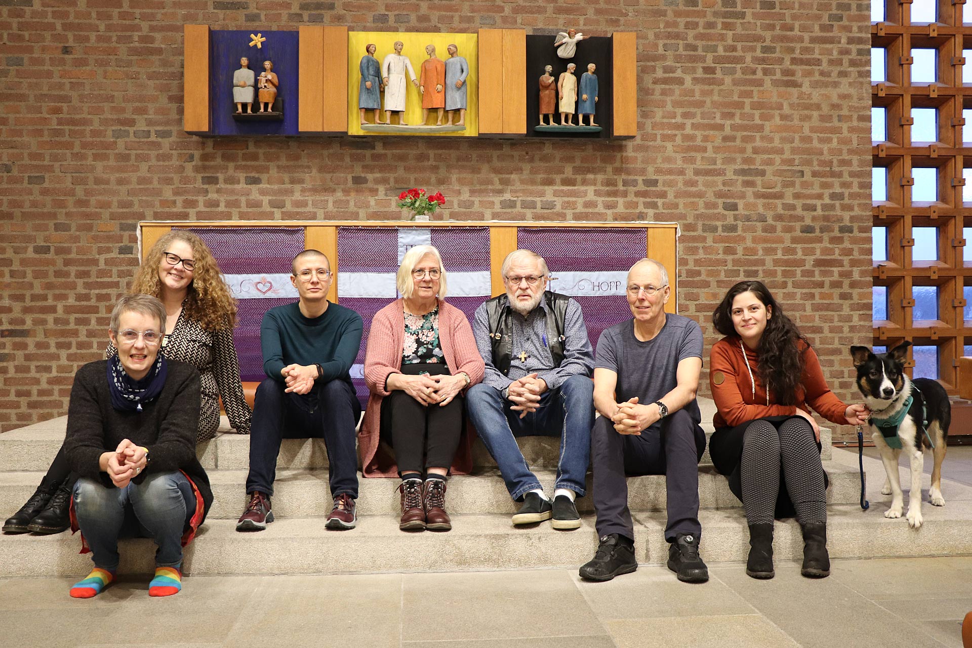 Sju personer och en hund sitter vid altaret i Härlanda kyrka. 