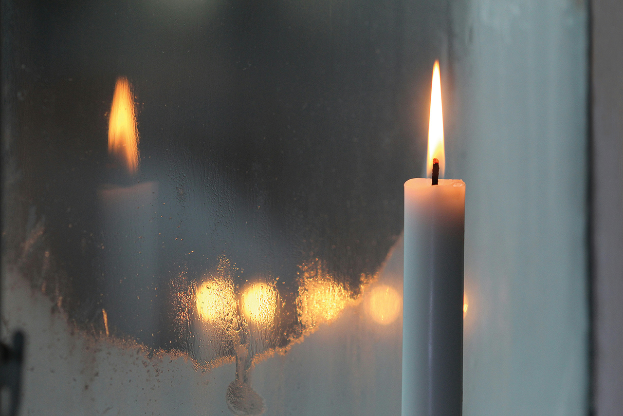 Ett tänt stearinljus speglas i ett fönster.