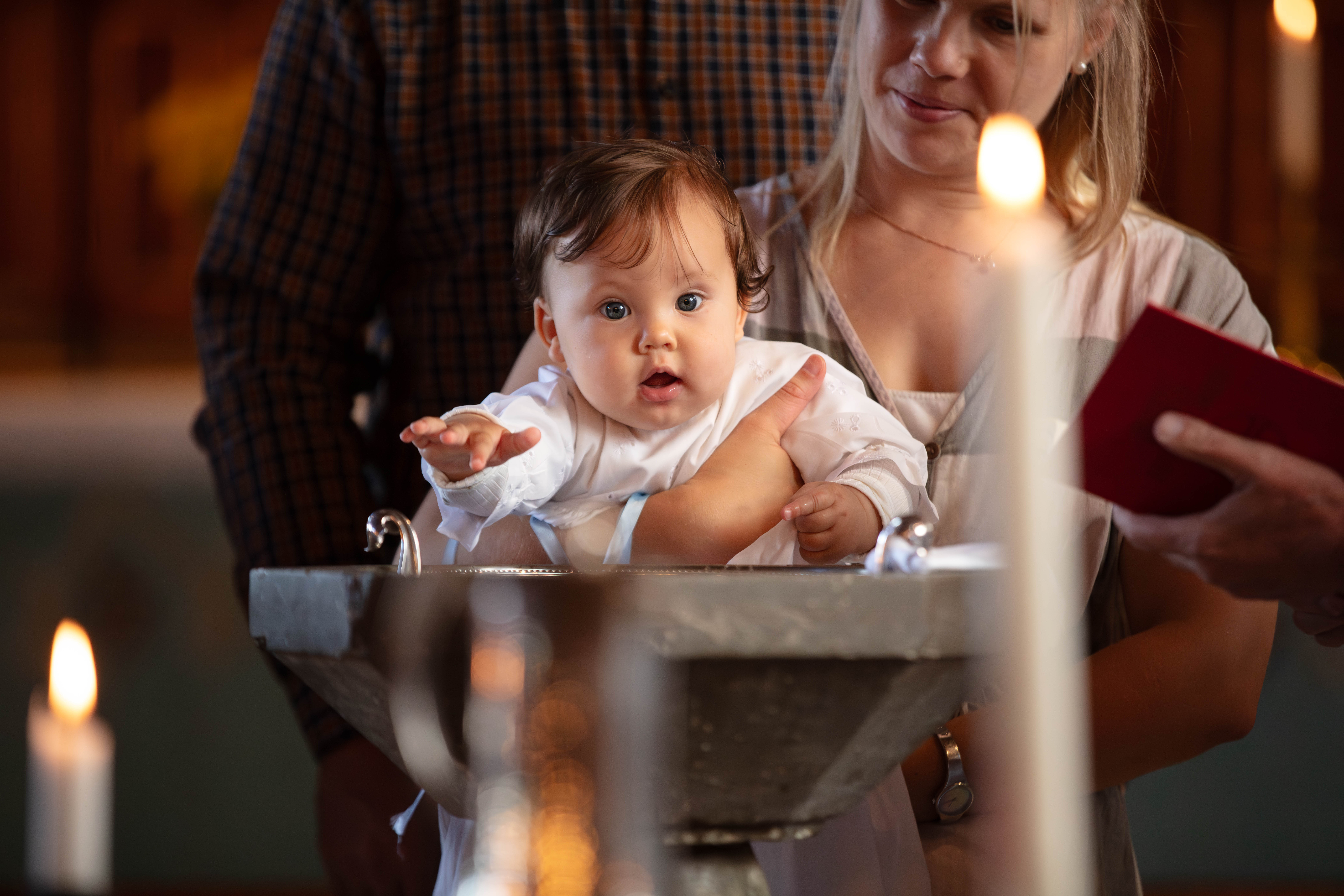 Dopbarn som hålls i mammans famn, vid dopfunten. I förgrunden står dopljuset tänt.
