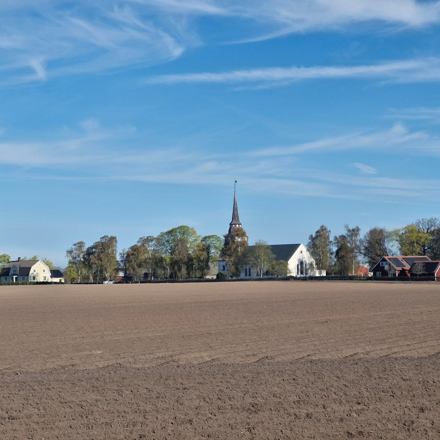 Hasslövs kyrka med blå himmel ovanför och pjöjd åker framför