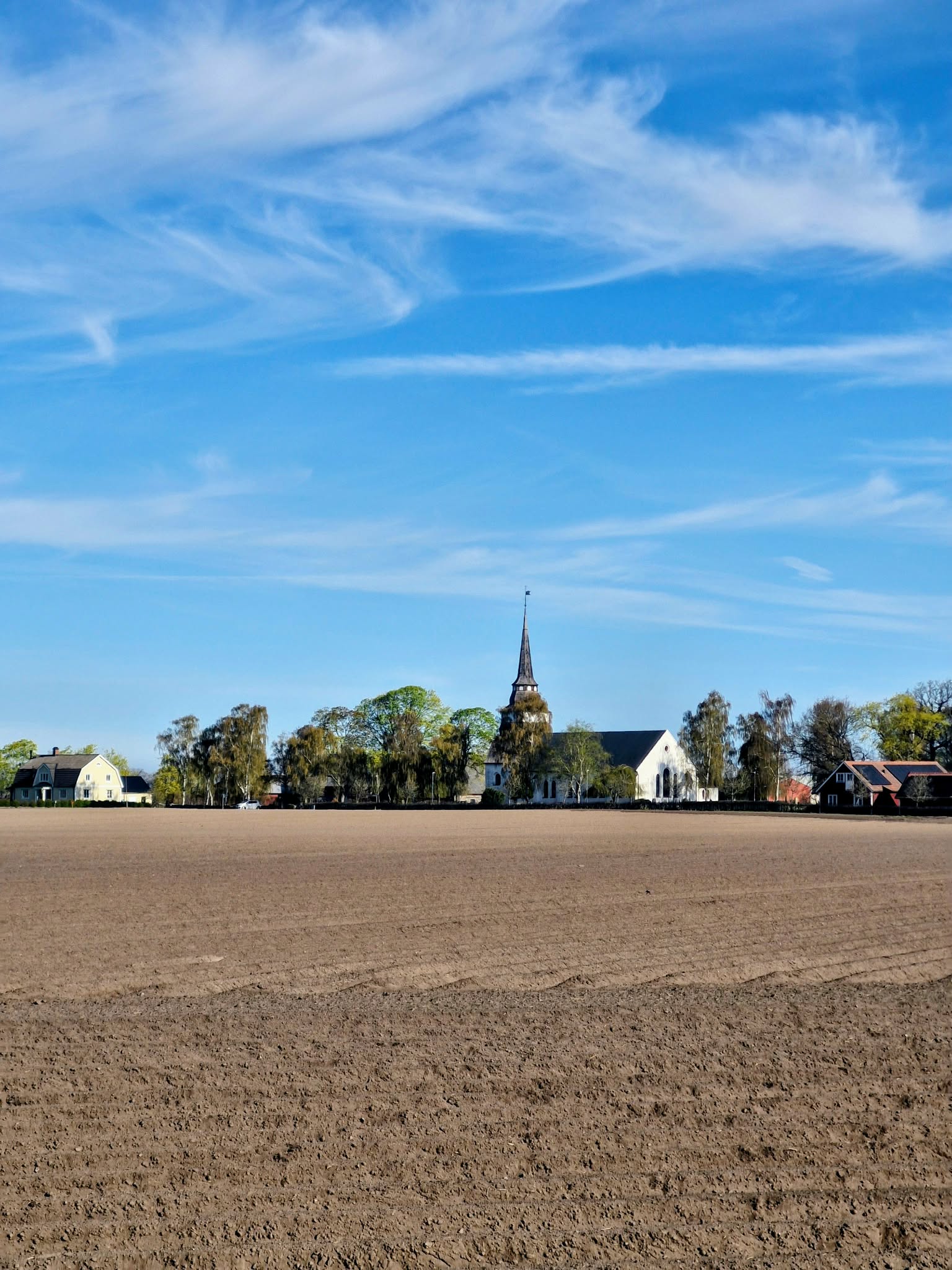 Hasslövs kyrka med klarblå himmel ovanför och nyplogad åker framför
