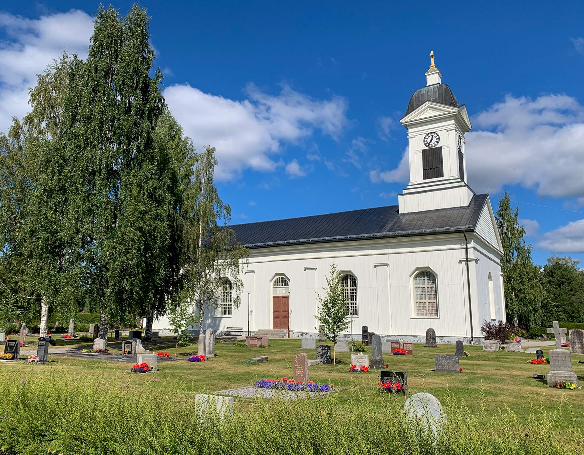 Vit träkyrka med klocktorn på själva huskroppen.