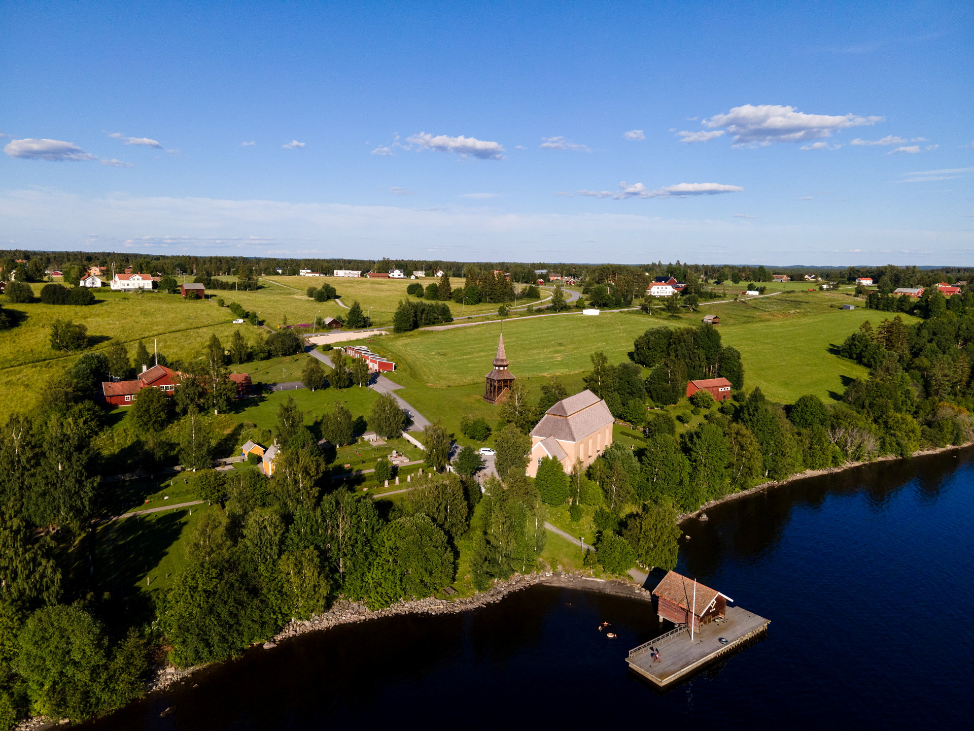 En vybild över en kyrka, klocktorn och en strand vid en sjö.