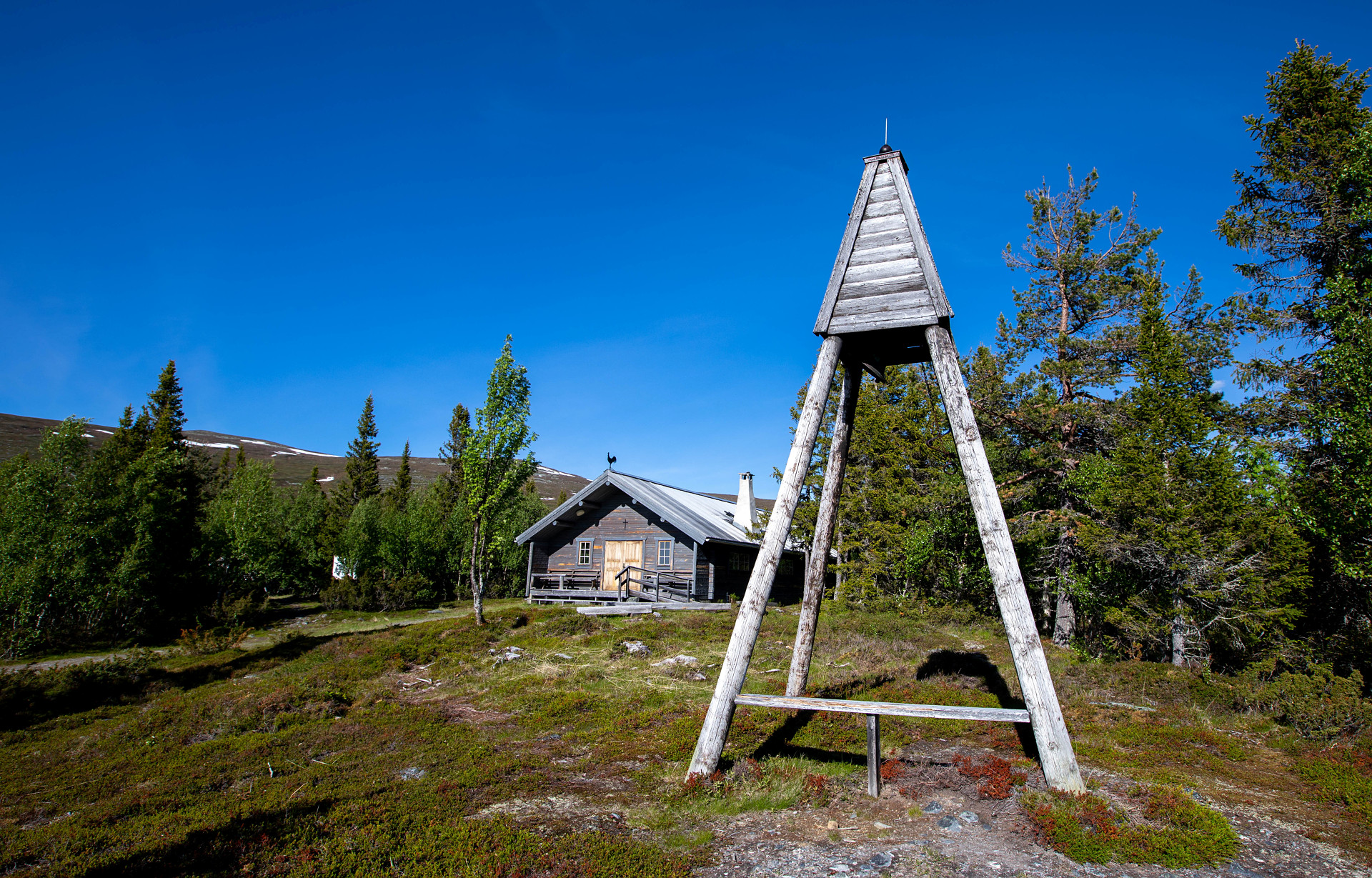Kapell i fjällmiljö. Klockstapel i förgrunden.