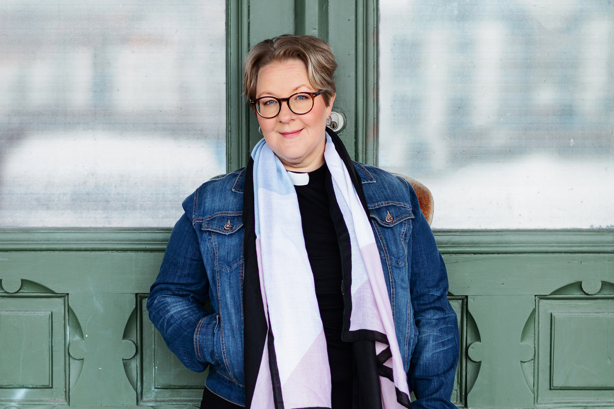 En kvinna i jeansjacka och skarf, med prästskjorta.