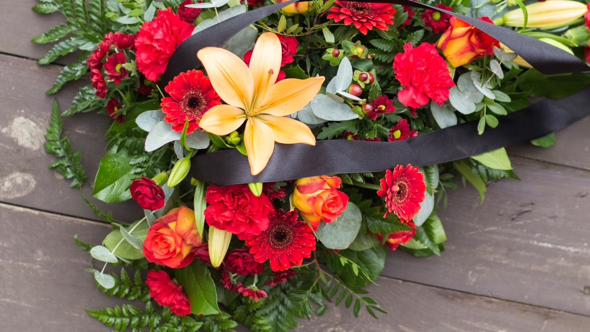 En bukett med röda och gula blommor som ligger på ett trägolv.