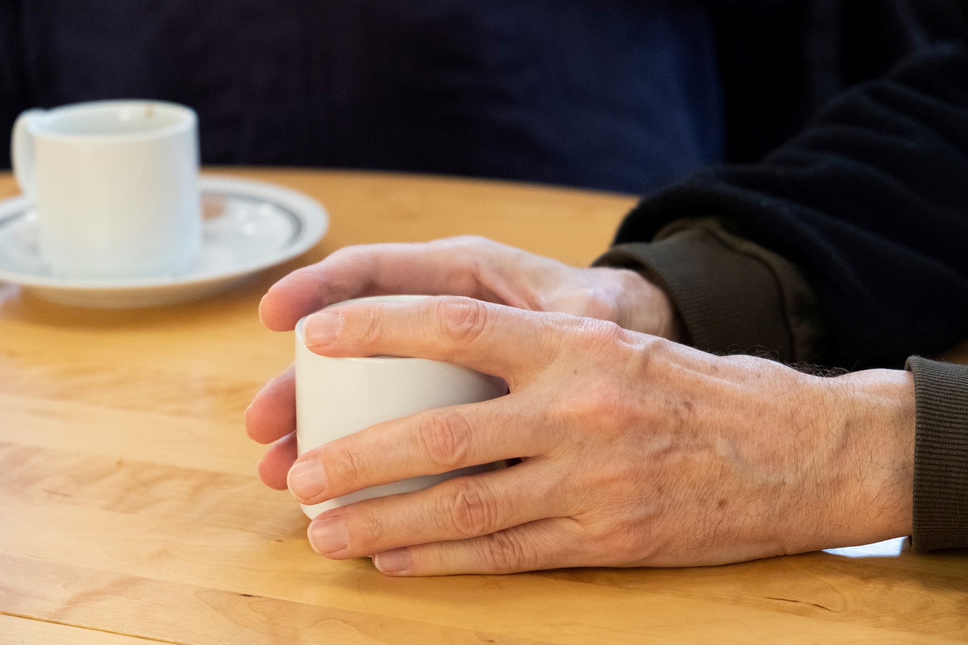 Någon håller händerna runt en kaffekopp på bordet.