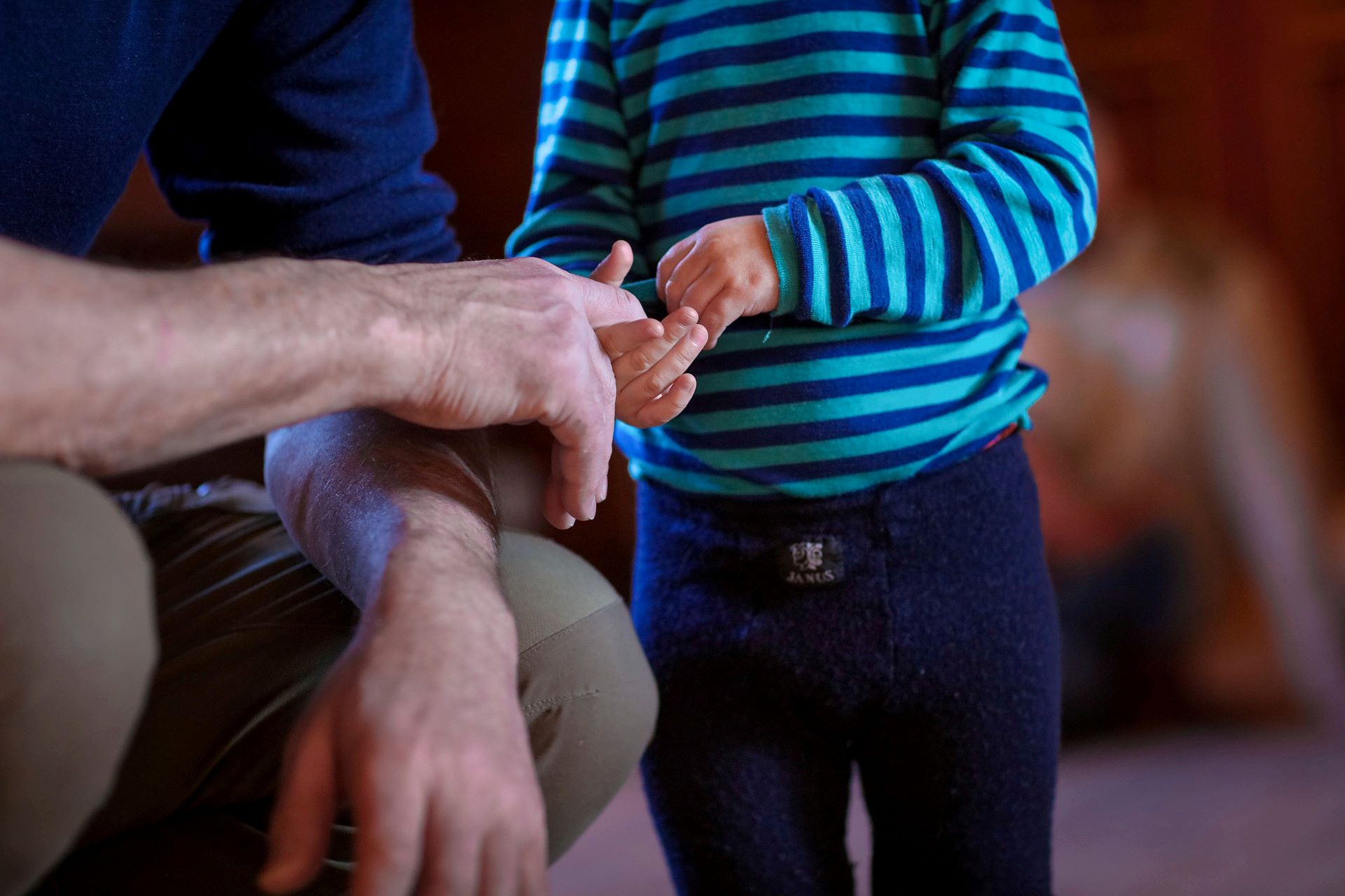 En man sitter på huk bredvid ett litet barn. Barnet håller om hans finger.