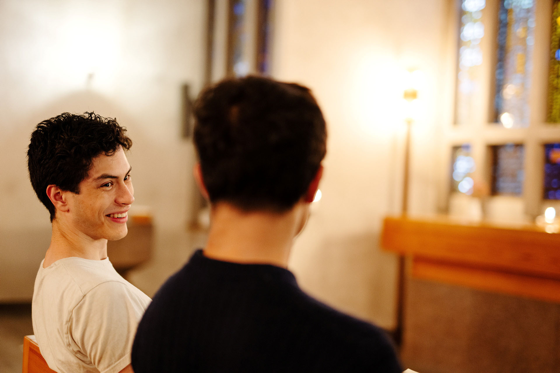 Två unga vuxna killar sitter i en bänk och pratar med varandra.