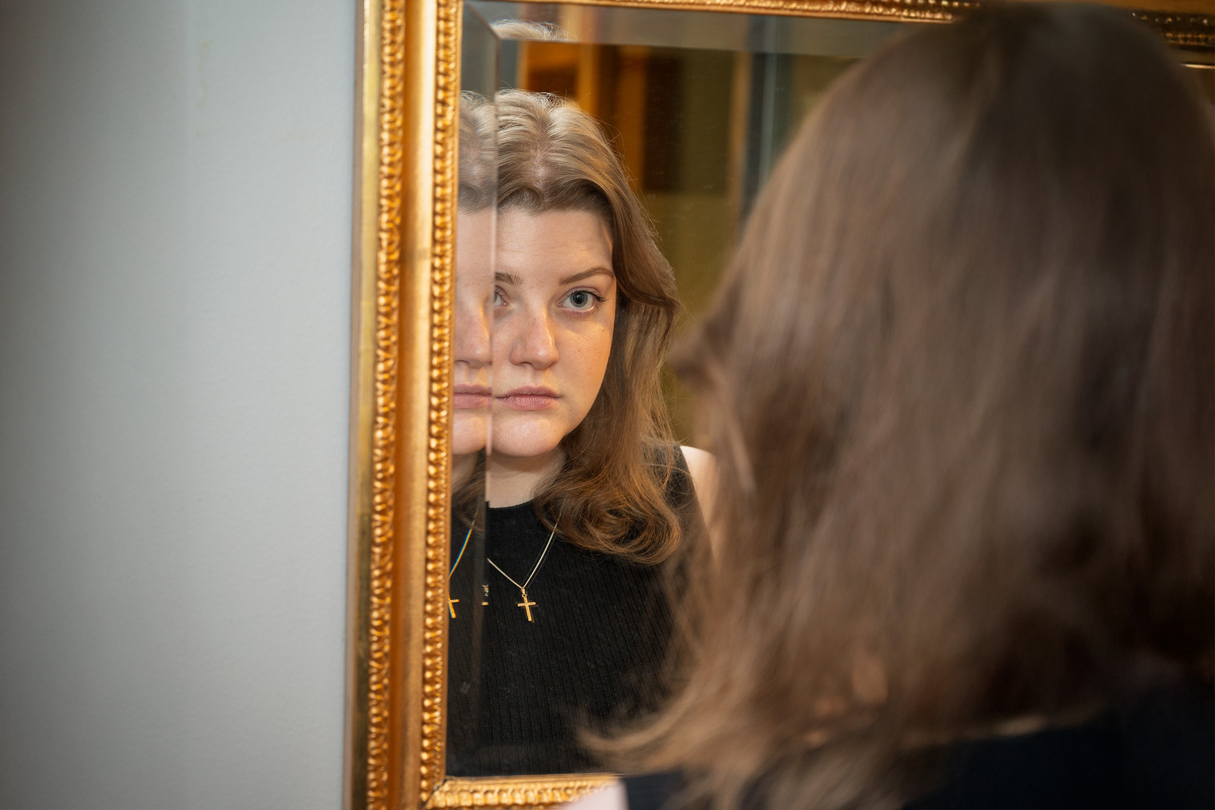 En ung kvinna med lite ledsna ögon ser sig i spegeln.