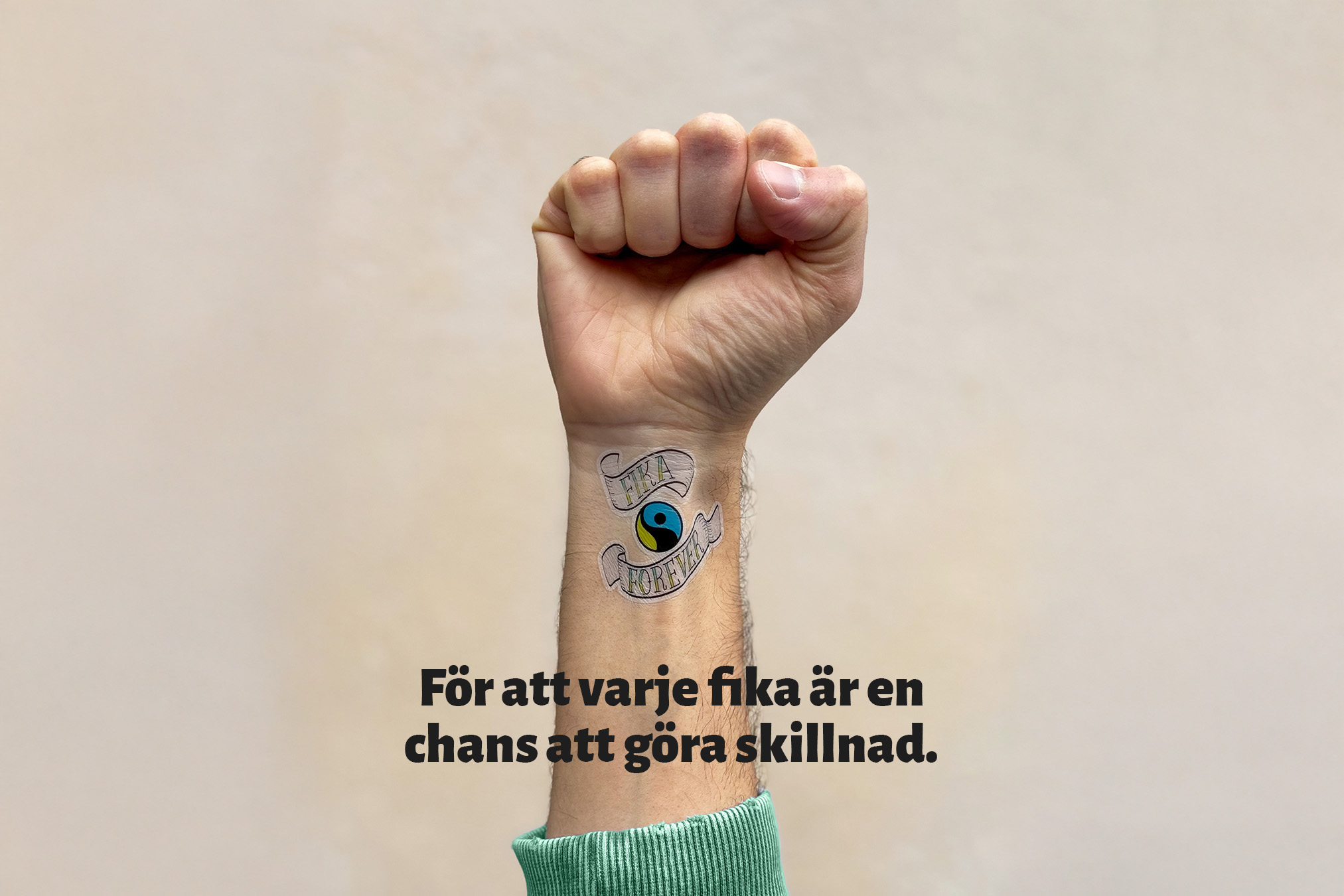 En knyten hand pekar upp mot skyn. På handleden syns en tatuering av Fairtrade-logotypen, en yin/yang-form och texten "Fika Forever". Nedanför tatueringen står texten "För att varje fika är en chans att göra skillnad".