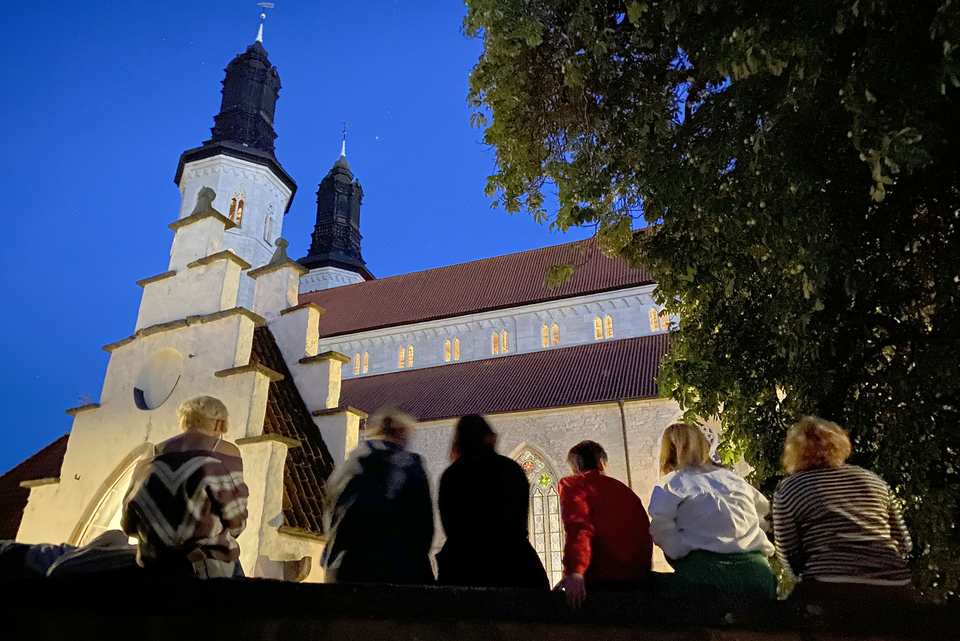 Ungdomar i domkyrkoförsamlingen sitter på en mur och kikar på domkyrkan.