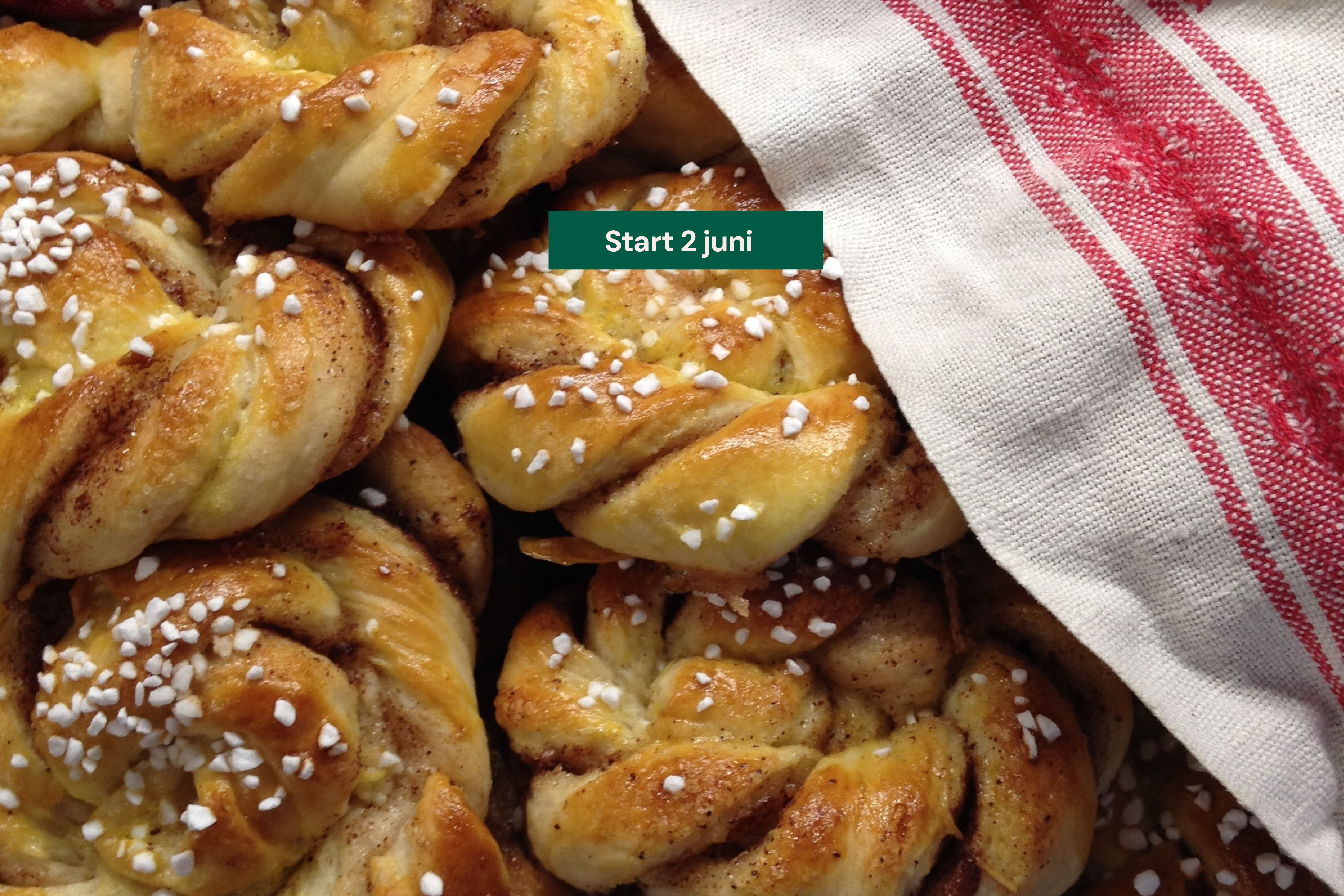 Bilden visar nybakta kanelbullar under en röd och vit bakduk.