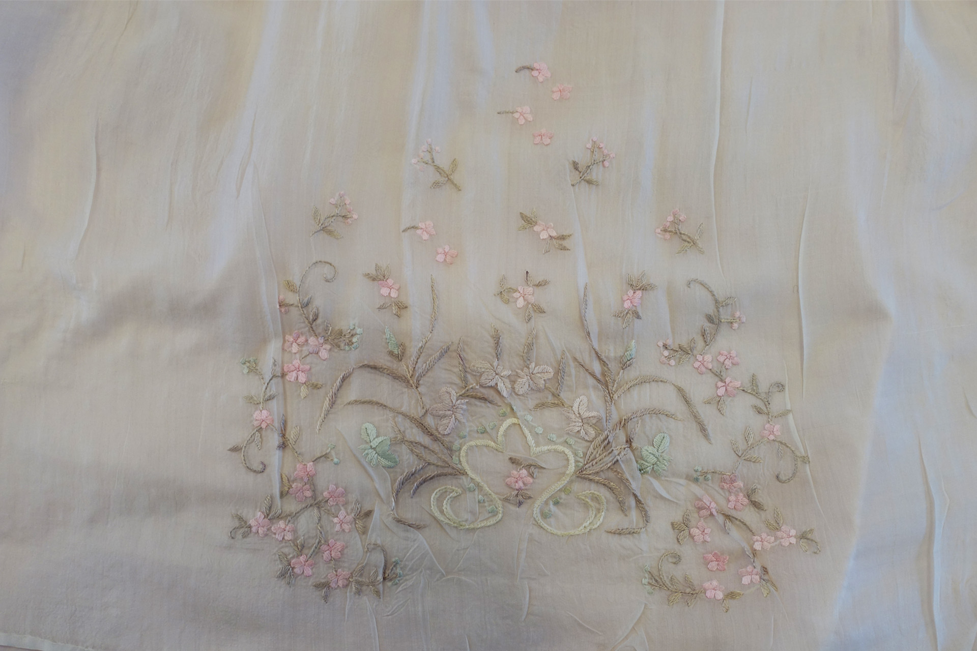 Fint mönster som är sytt på en av församlingens dopklänningar. Mönstret är en massa små blommor i rosa och blad i grönt. 