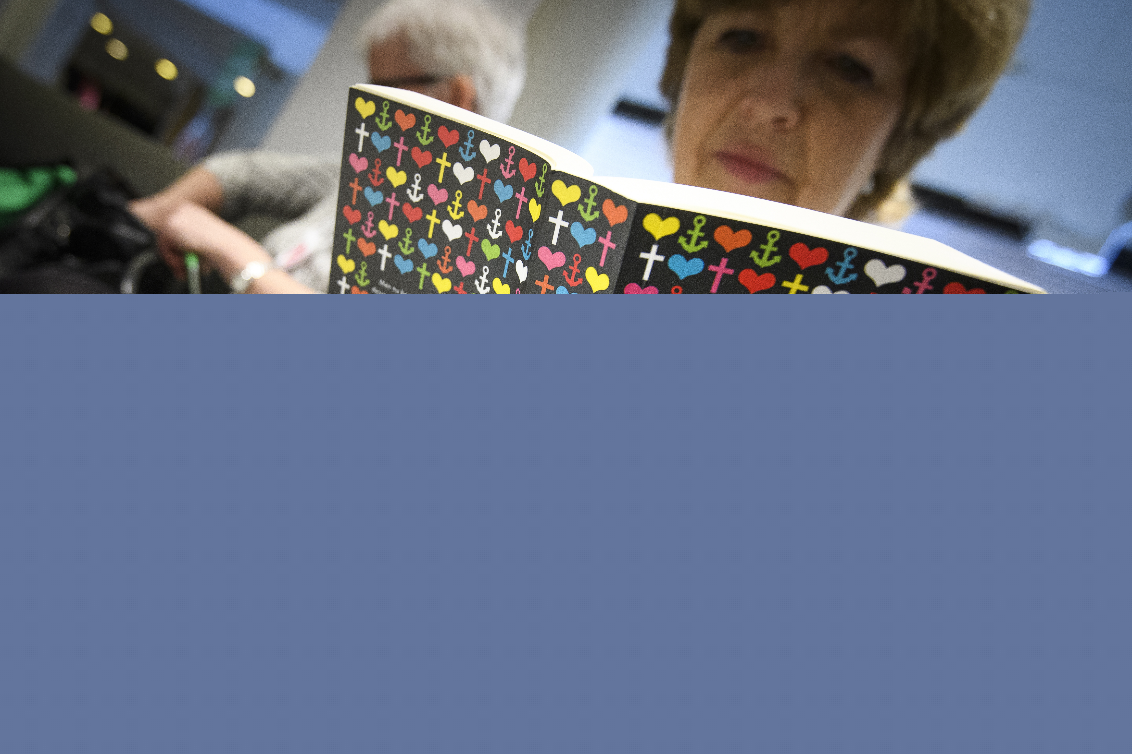 En kvinna sitter och läser Bibeln. I bakgrunden syns en kvinna till. 