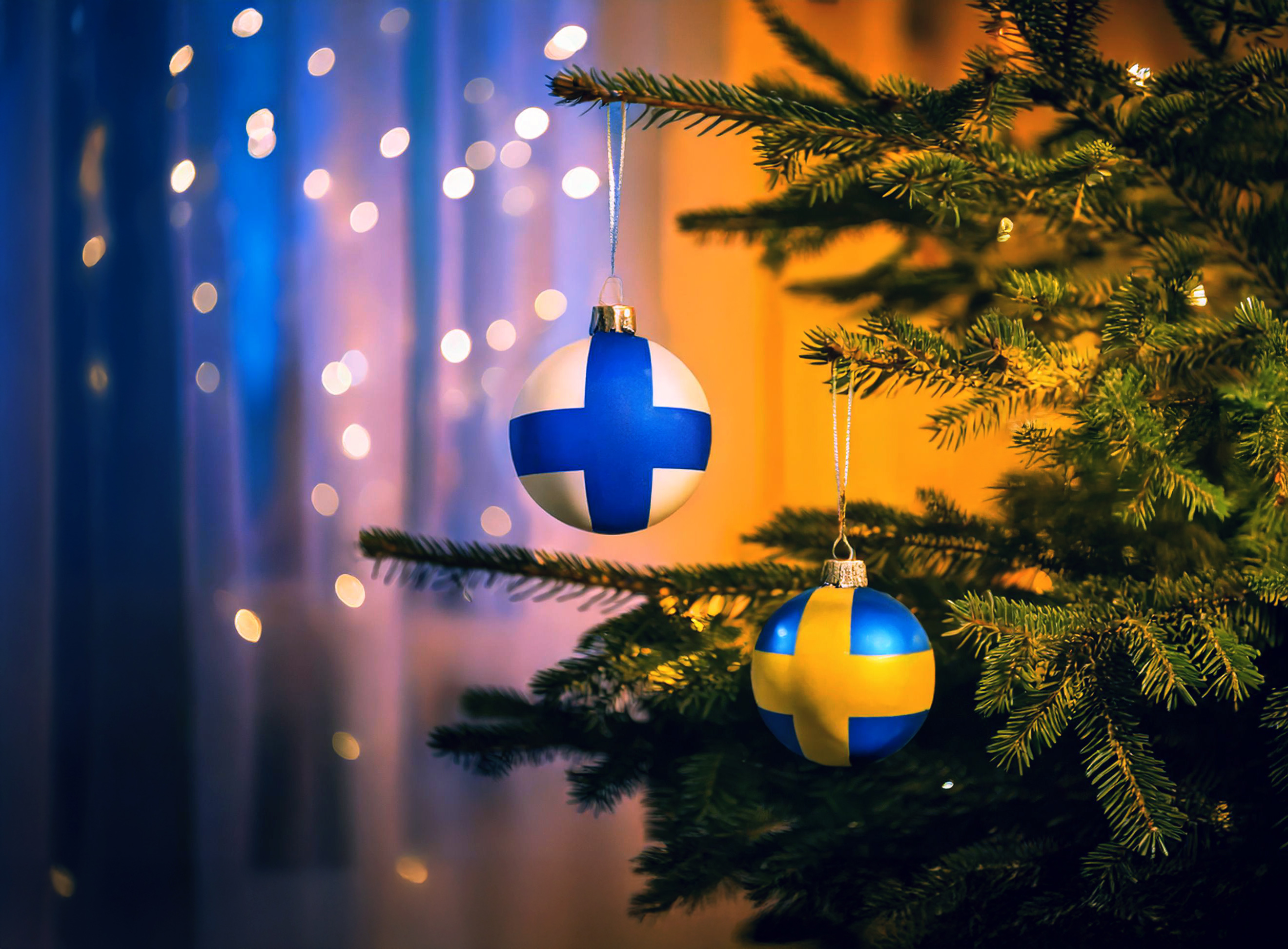 Två julkulor hänger i en gran, en med finska flaggan och en med den svenska.