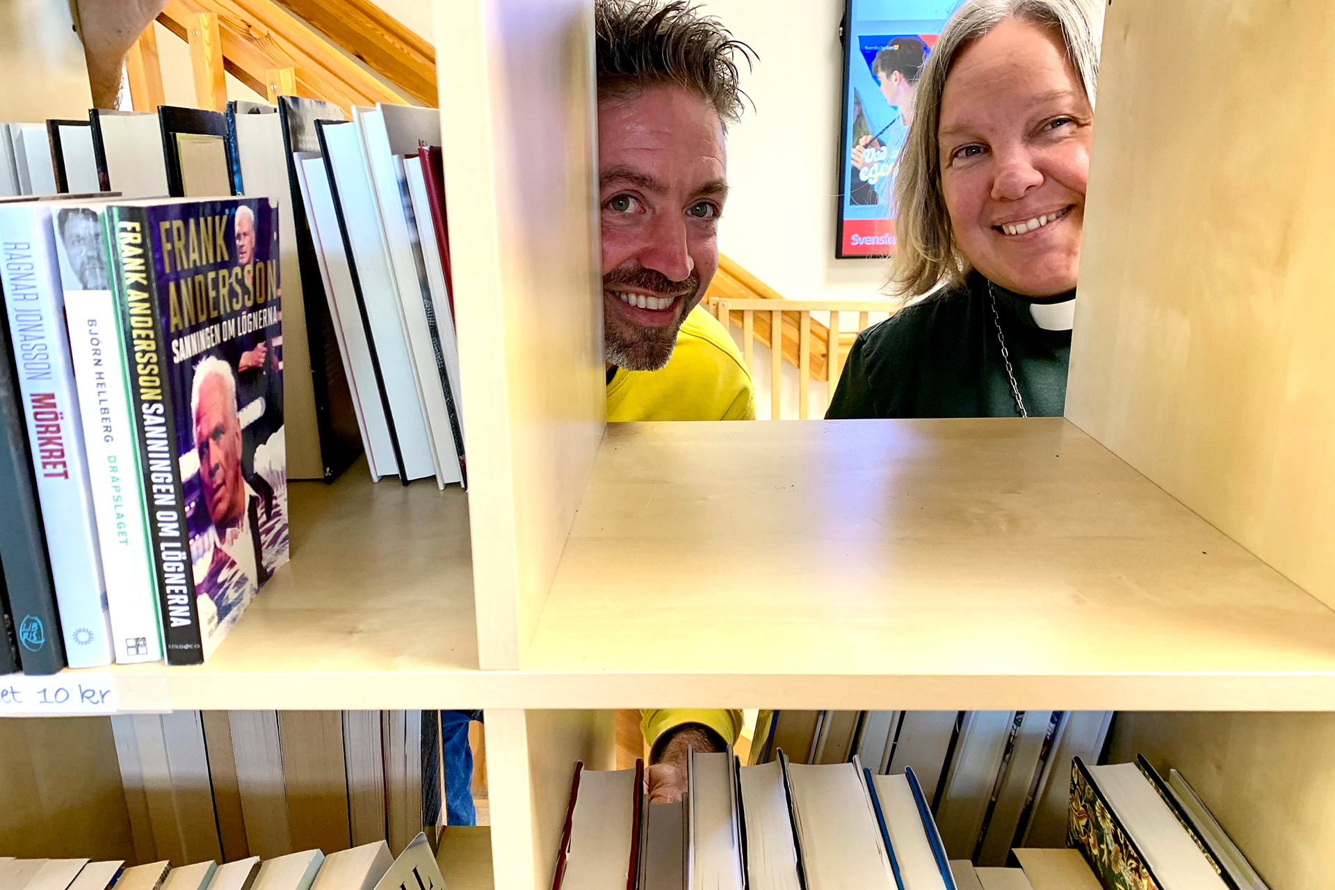 En man och en kvinna kikar genom en bokhylla.