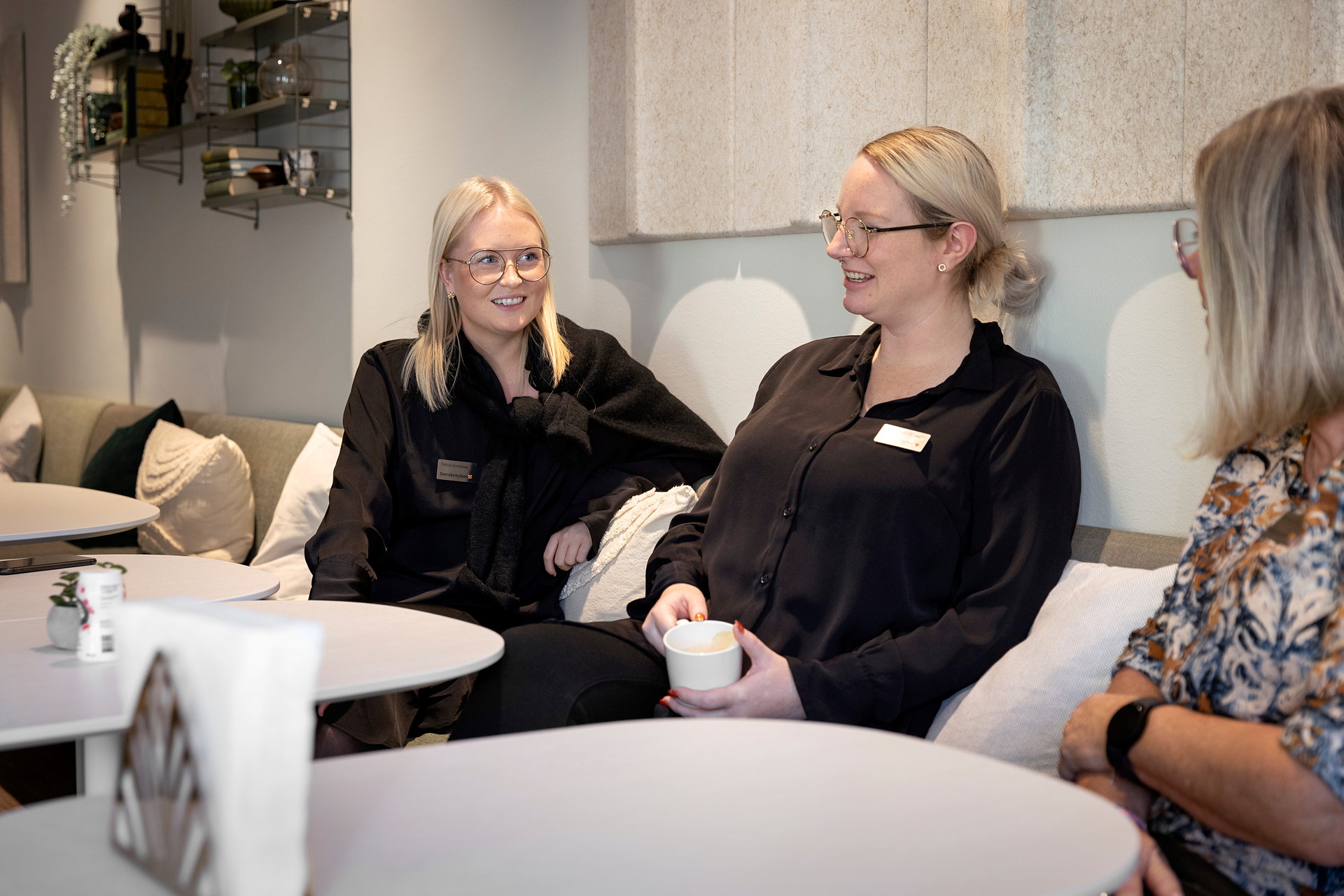 Tre kvinnor pratar och skrattar i en kontorssoffa.