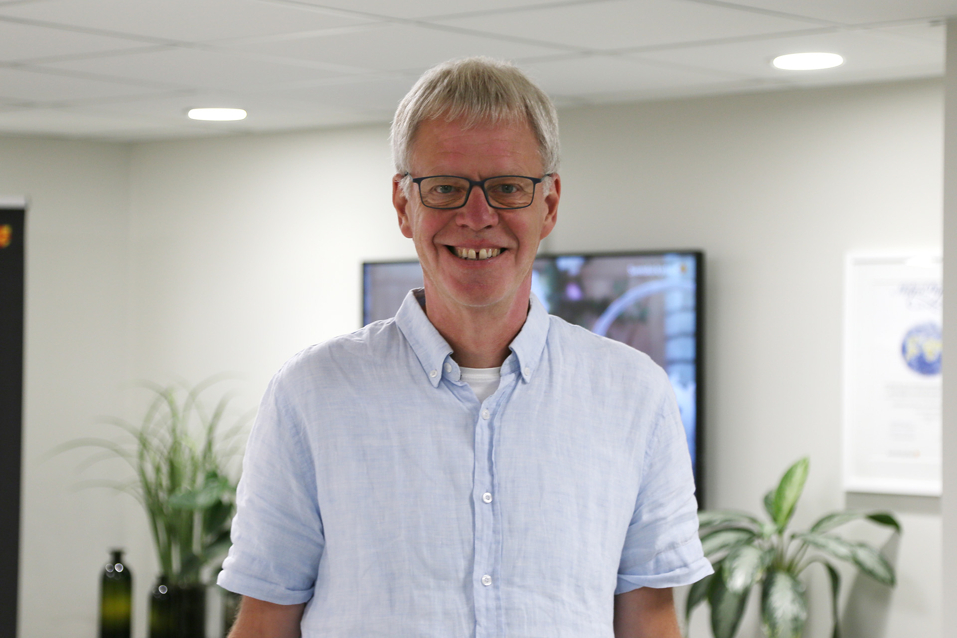 En lång leende man, med grått hår och glasögon, klädd i kortärmad skjorta.