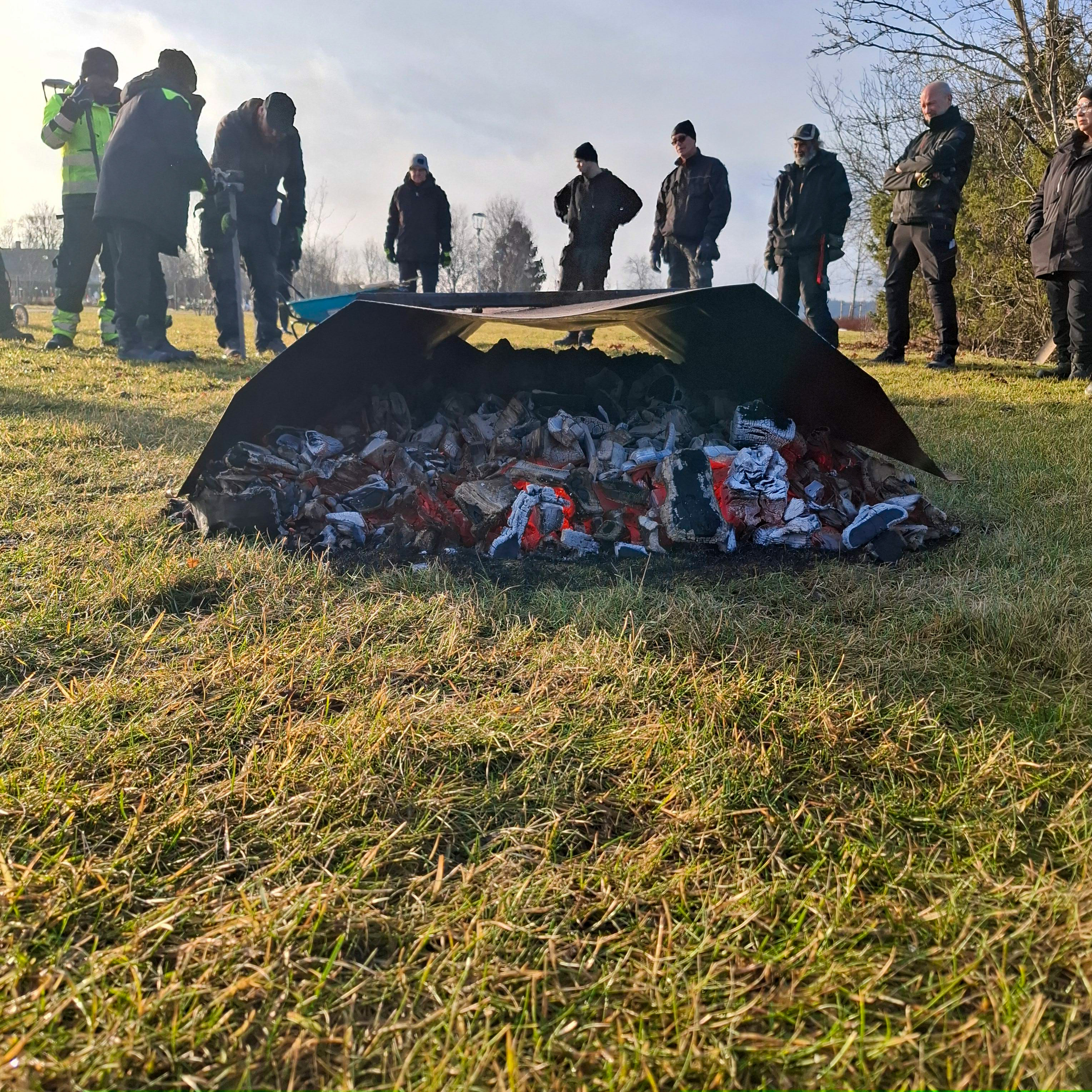 En bild som visar hur man under en beredskapsövning tinar upp tjälen i jorden med kol för att kunna gräva en grav utan tillgång till el eller diesel.