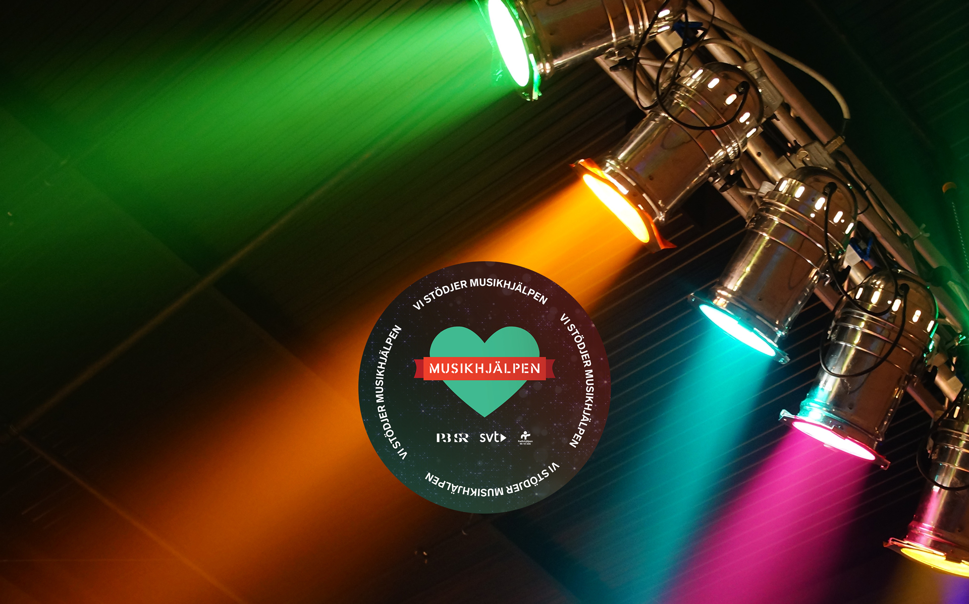 Spotlight i olika färger lyser ner mot logotypen Musikhjälpen.