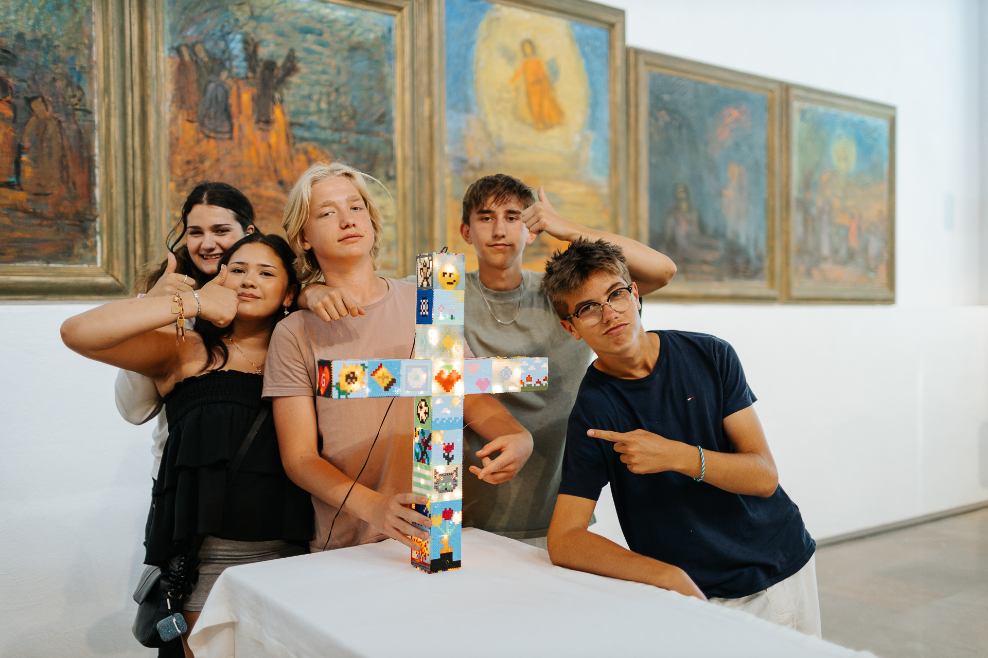 Fem ungdomar som gör tummen upp vid ett kors gjort av pärlplattor