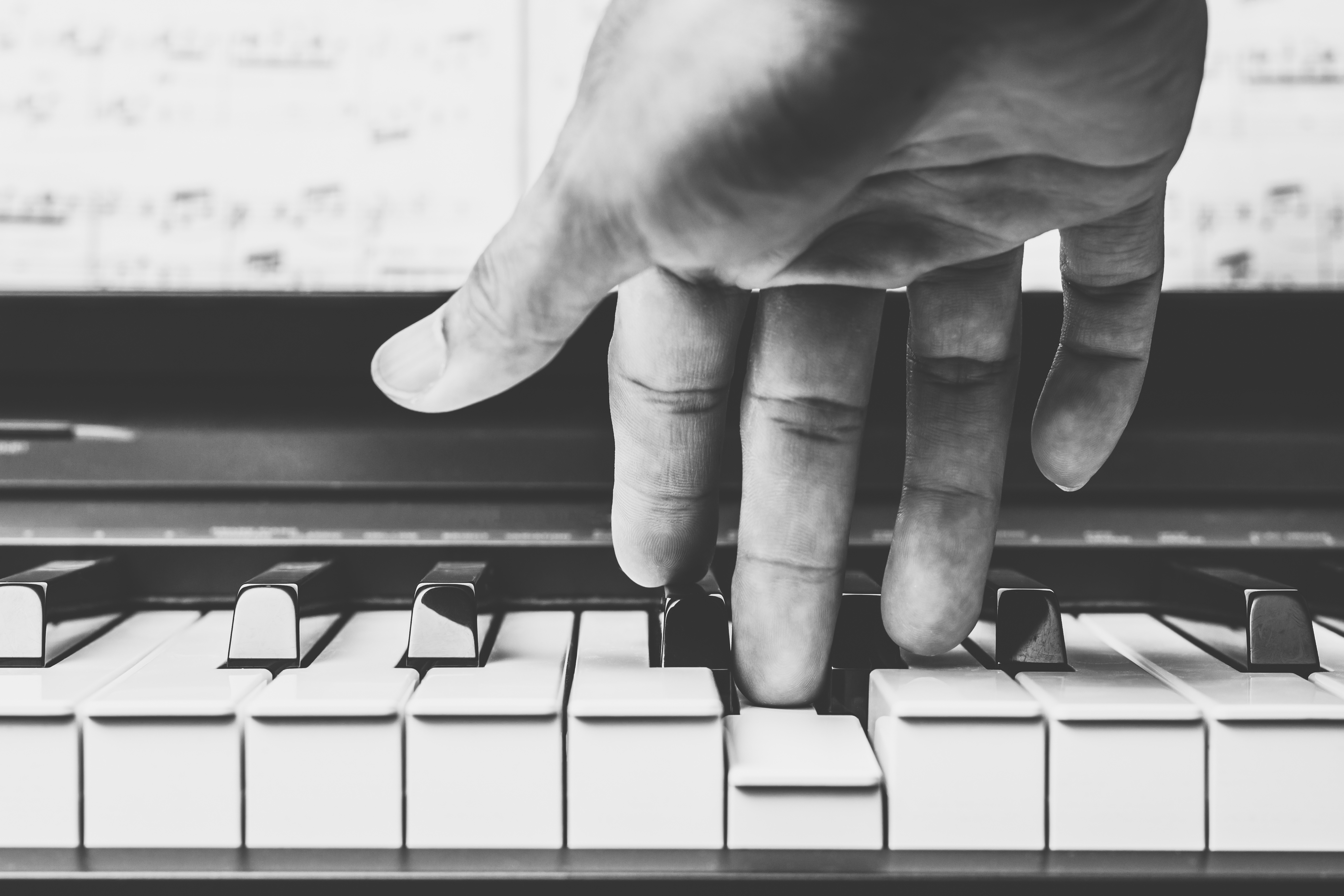 Svartvit bild av en hand som trycker ner tangenter på ett piano.