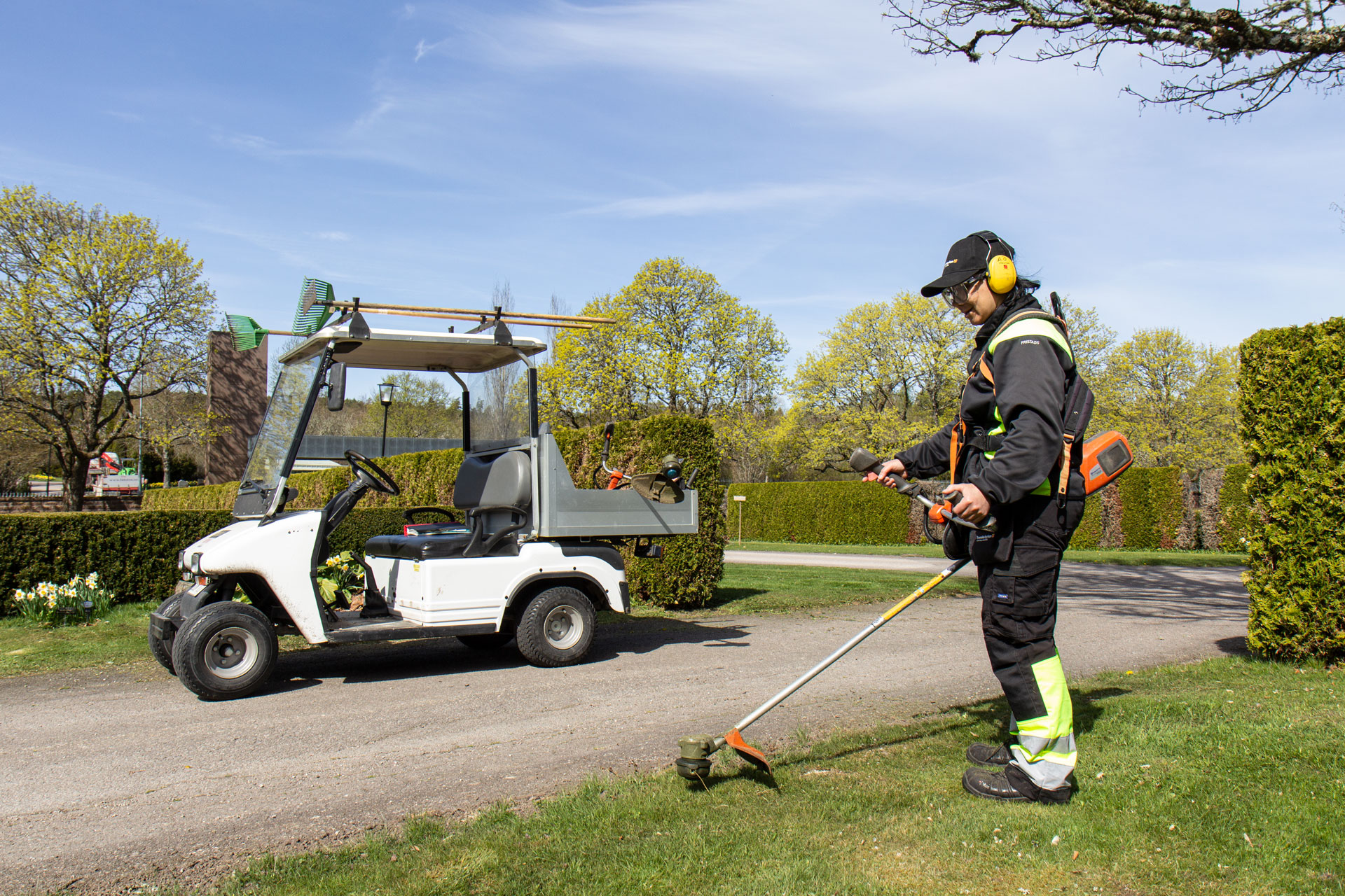 Kyrkogårdsarbetare trimmar gräset på Sigelhults kyrkogård.