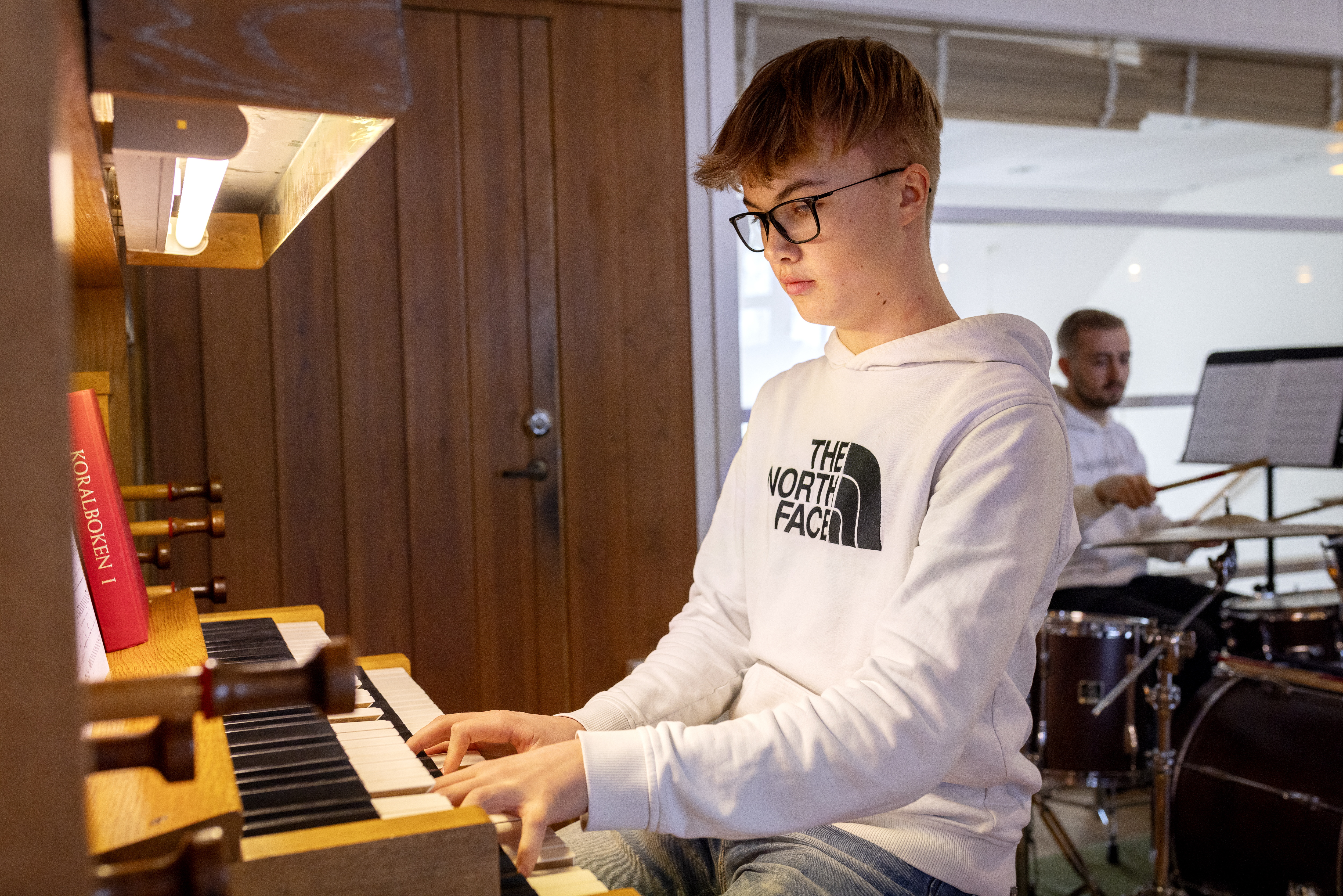 En pojke med vit sweatshirt med huva sitter och spelar orgel.
