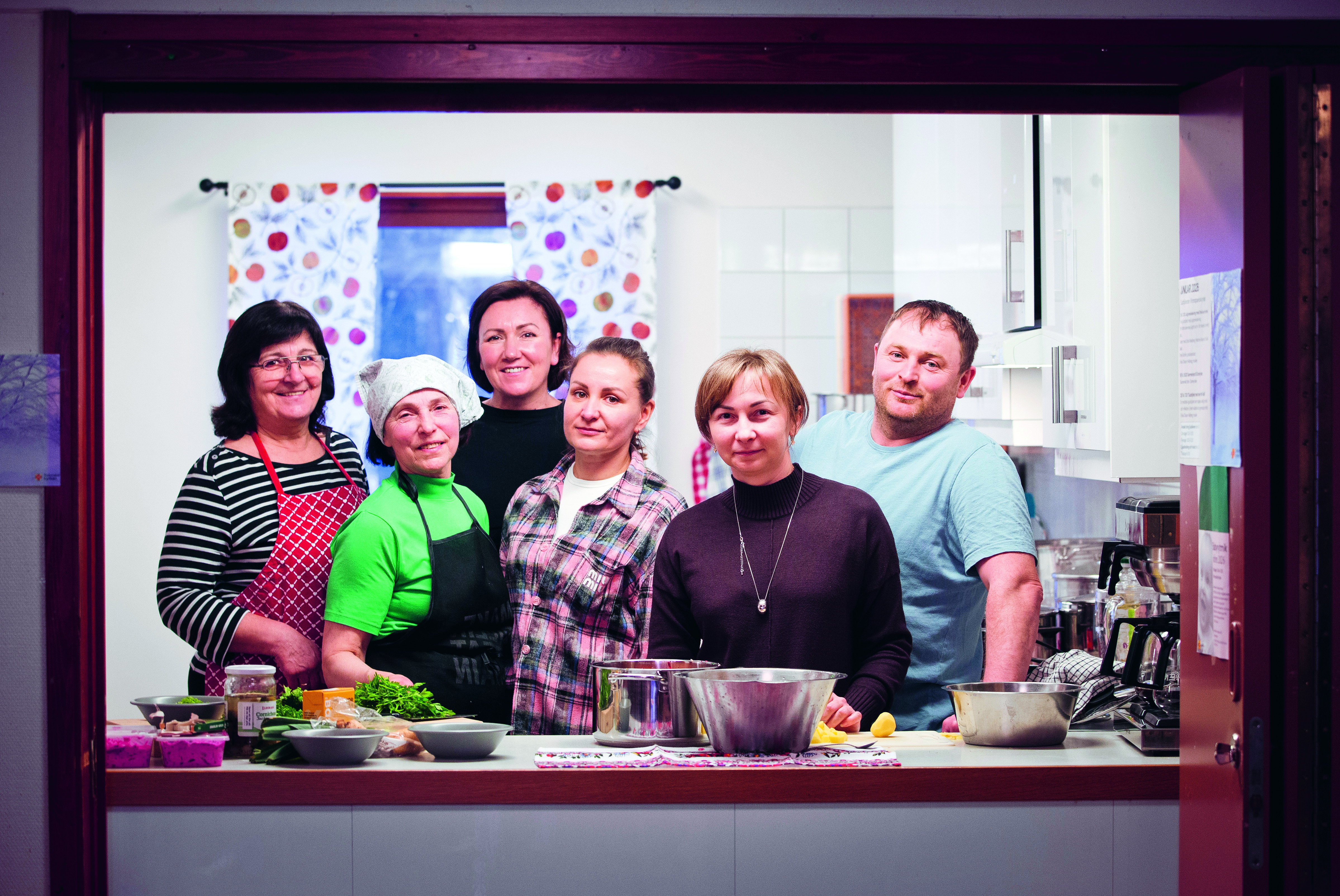 Sex personer från ukraina står i Kronoparkskyrkans kök vid en bänk med olika ingredienser. 