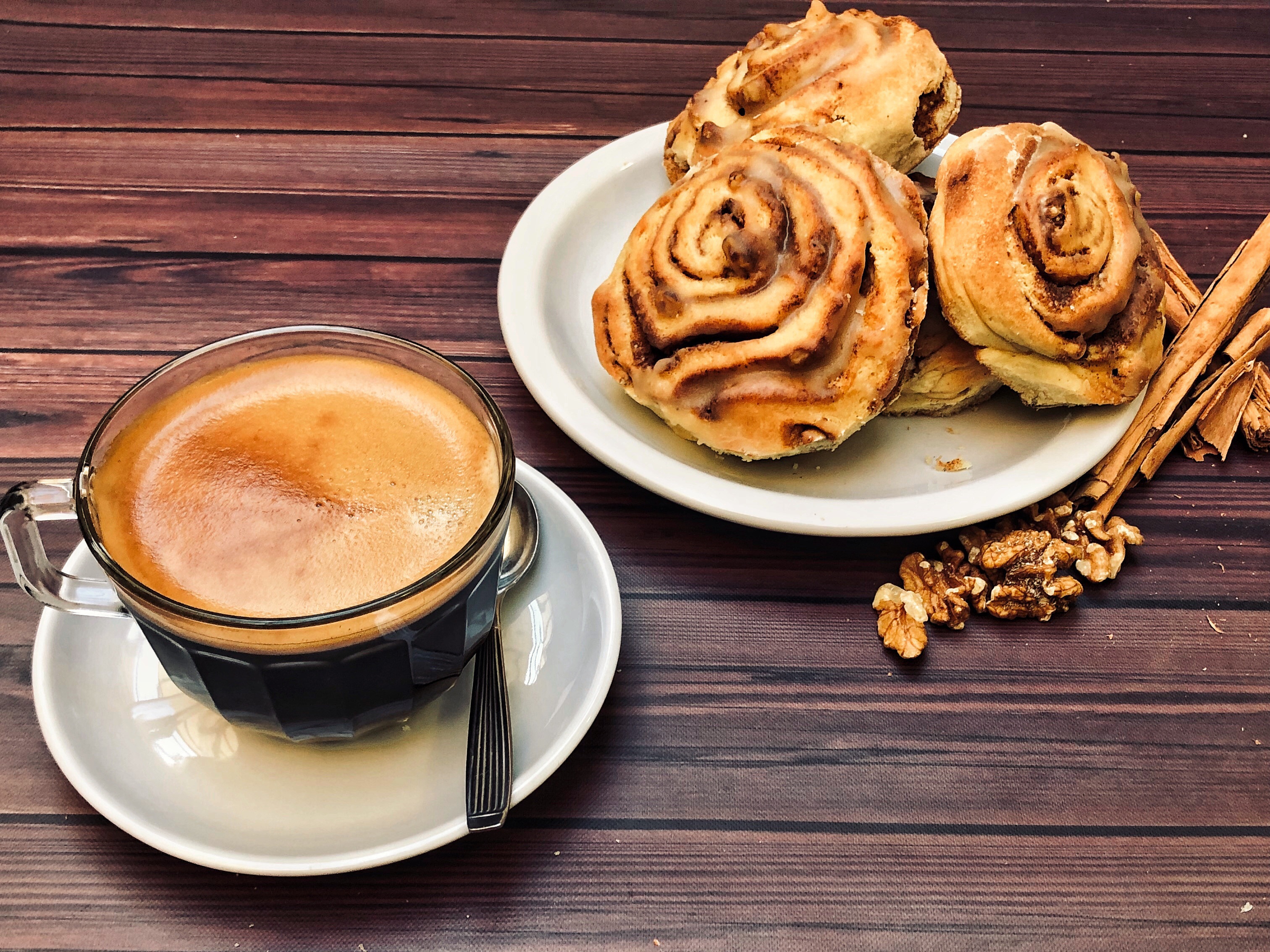 Kaffe i glaskopp och tre kanelbullar på ett vitt fat bredvid