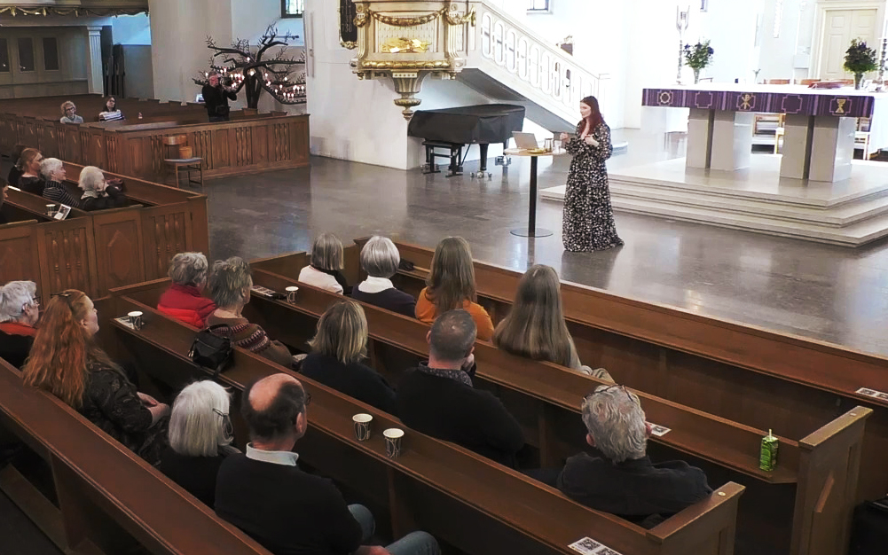 Inne i domkyrkan i Karlstad. Åhörare sitter i bänkar i förgrunden och föreläsaren Emma Engdahl föreläser.