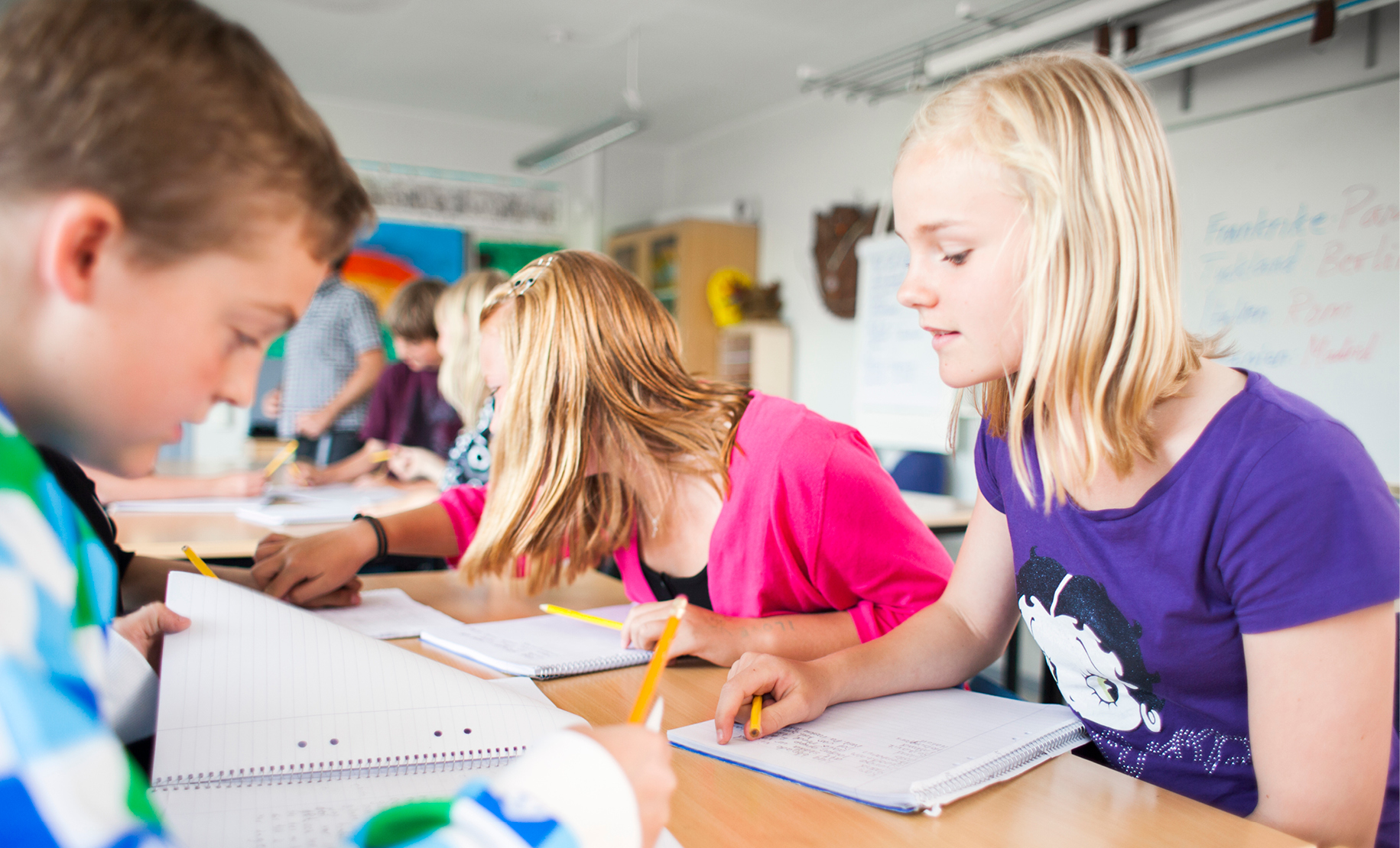Mellanstadiebarn gör läxor vid ett bord. 