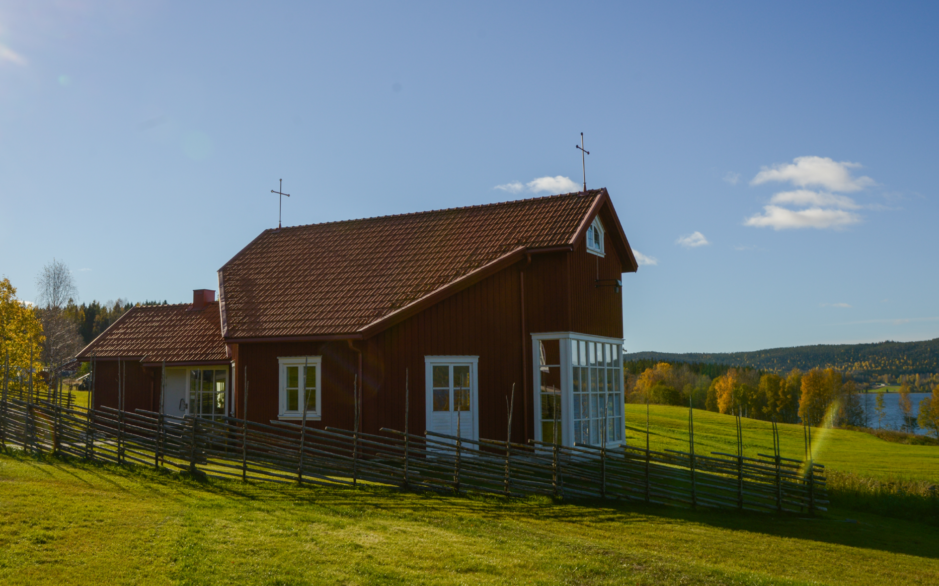 Ett rött hus och grön gräsmatta i solsken.