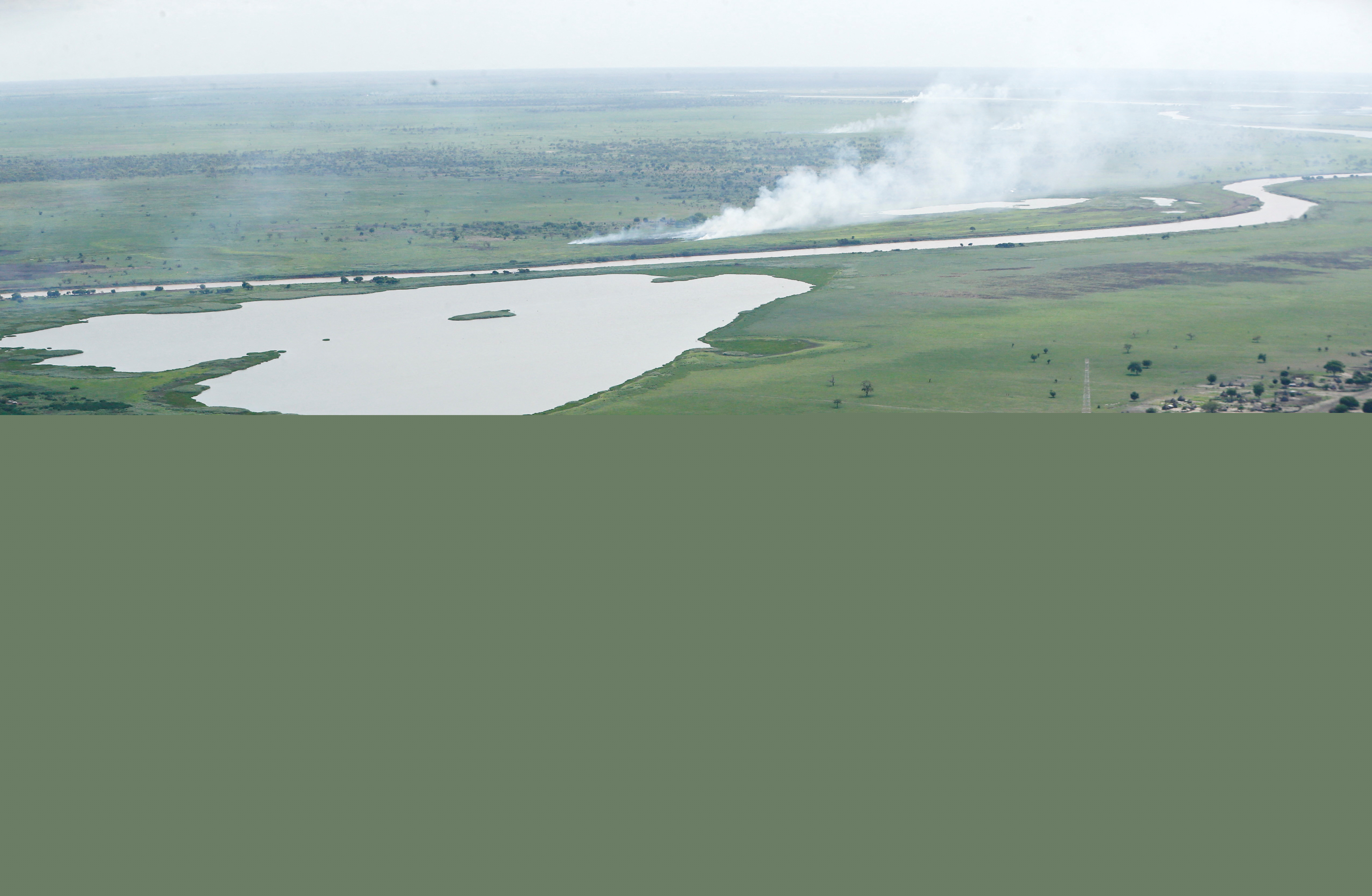 Platt grönt landskap med by och en flod och rök som stiger på avstånd.