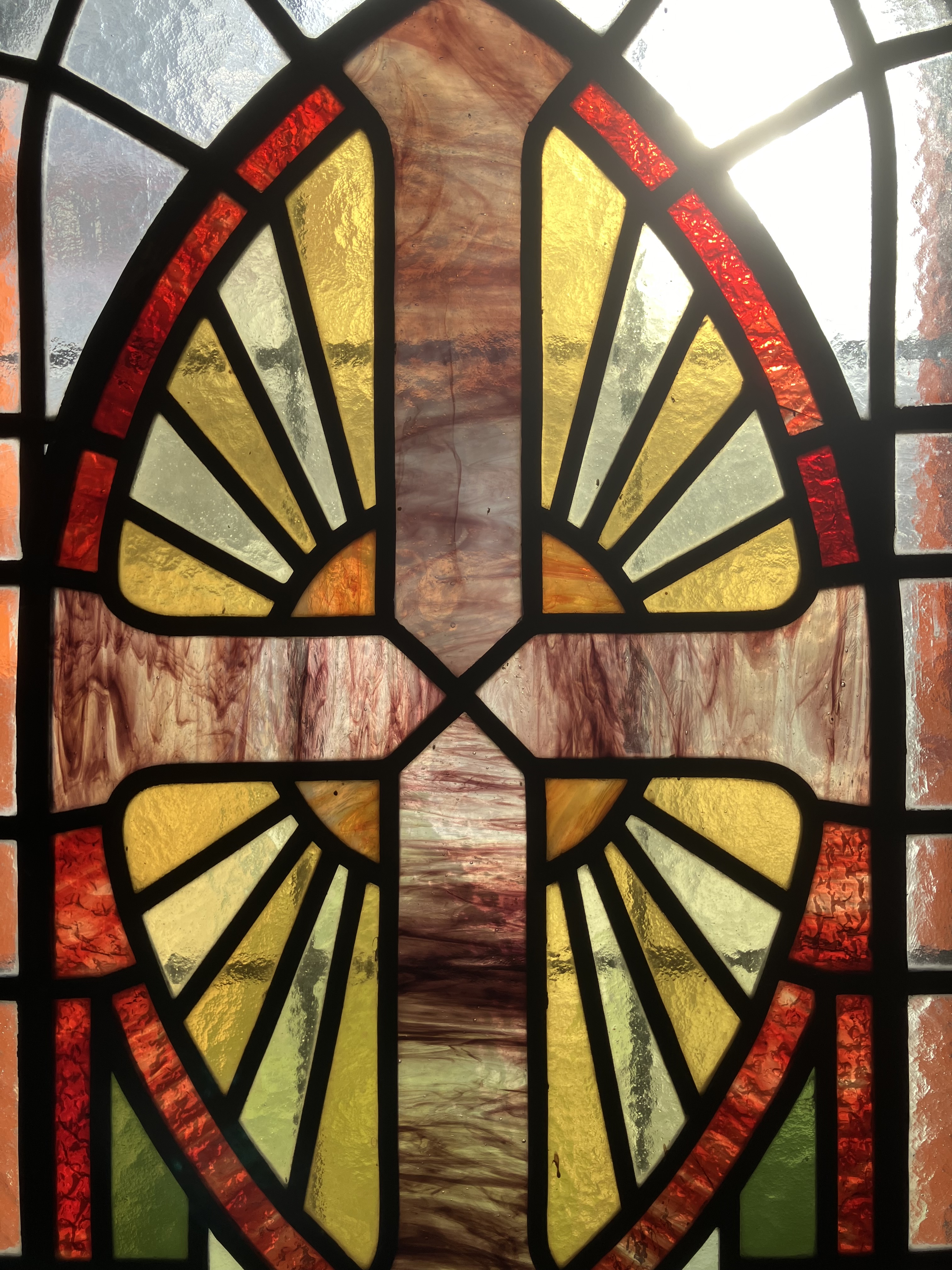 Bild av blyinfattat glasfönster, föreställande ett kors med solen bakom.