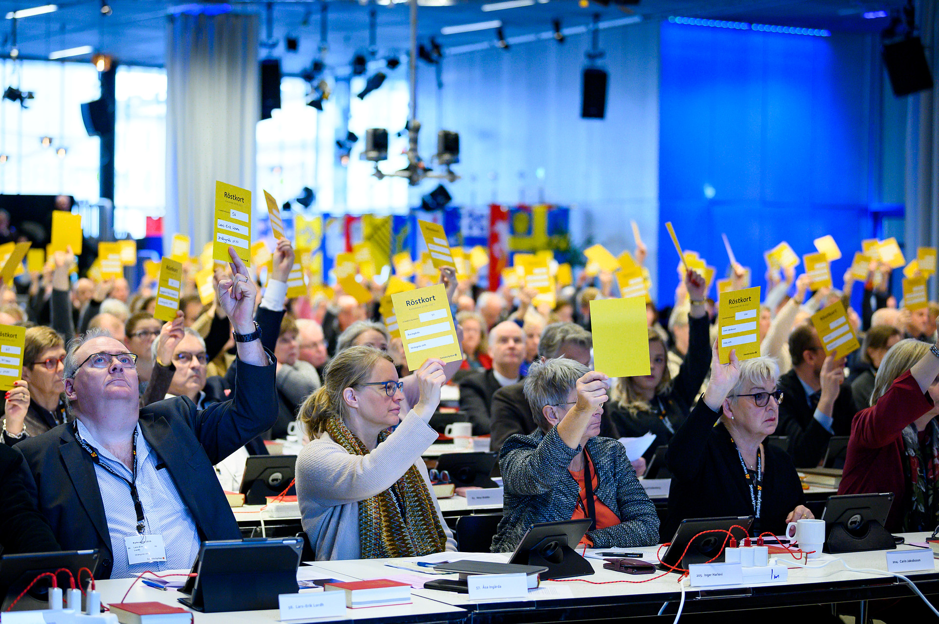 Ledamöter i kyrkomötet röstar genom att hålla upp  gula  lappar i kyrkomötets andra session 2019