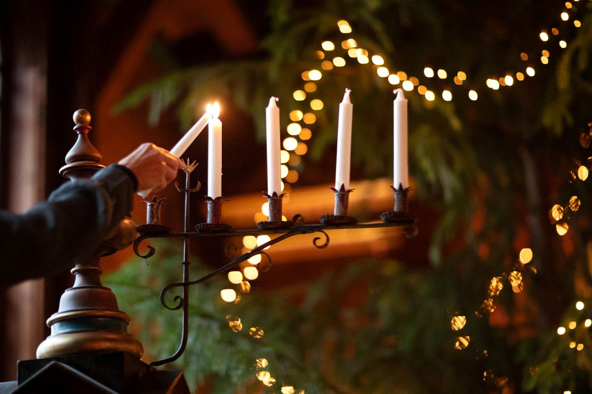 Hand tänder första ljuset i adventsljusstake med gran bakom.