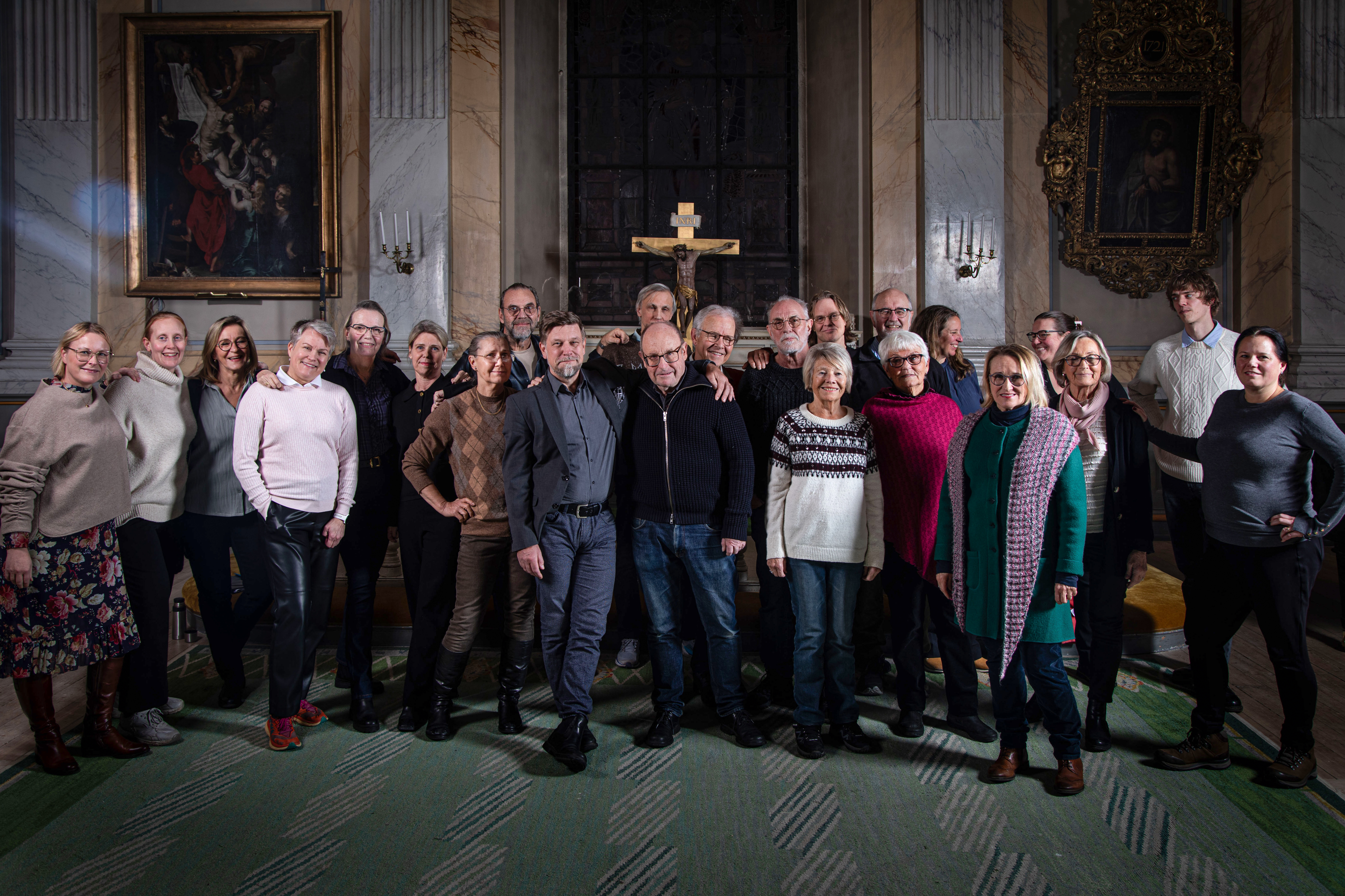 Kör med blandat män och kvinnor står i koret i kyrkan och ser glada ut.
